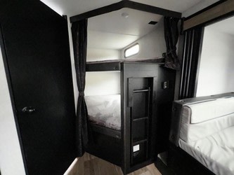 Inside your next RV rental: a modern interior featuring two bunk beds with privacy curtains, a dark door, and light seating.. Forest River Cherokee Grey Wolf 2022