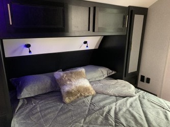 Cozy RV rental bedroom featuring a comfortable bed, overhead cabinets, and reading lights for relaxing travel.. Forest River Cherokee Grey Wolf 2022