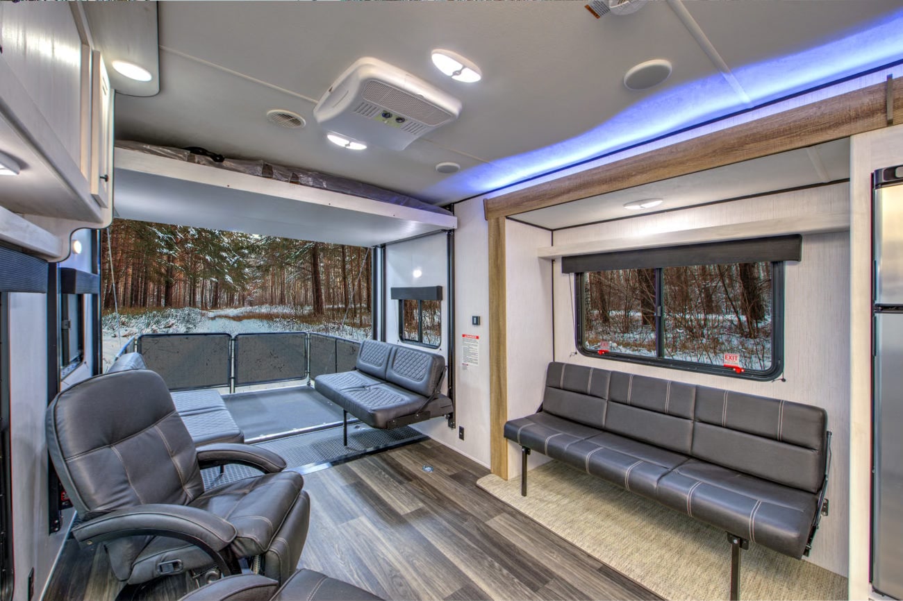 This RV rental's toy hauler interior offers versatile seating, a drop-down bed, and an open rear ramp to a serene snowy forest.. Heartland RVs Fuel Toy Hauler 2022