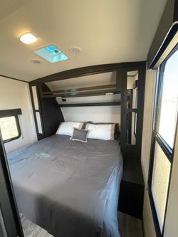 This RV rental features a modern master bedroom with a large bed, overhead storage, and natural light from side windows and a skylight.. Heartland RVs Fuel Toy Hauler 2022