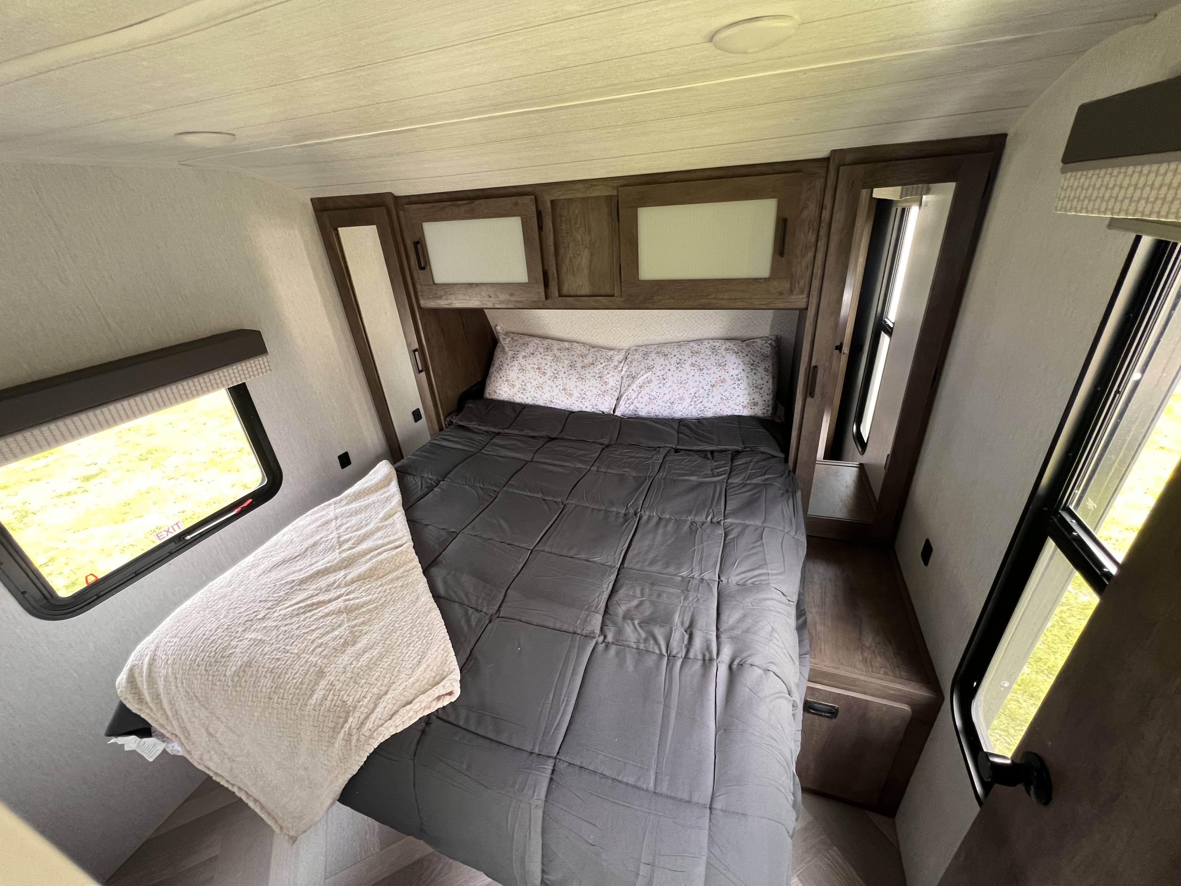 Comfortable RV rental bedroom featuring a bed, overhead cabinets, and windows for natural light.. Forest River Wildwood 2022