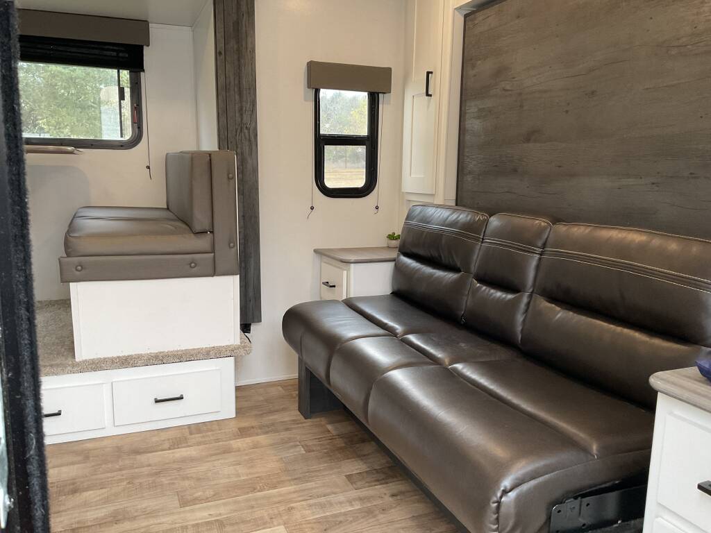 Inside a spacious RV rental: a plush brown sofa faces a raised dinette booth with storage, offering comfort.. Keystone Hideout 2022