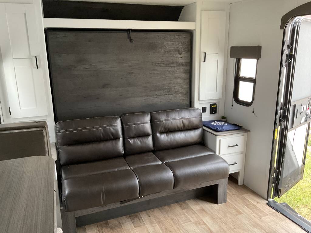 An inviting RV rental living area with a comfortable faux leather sofa, wall-mounted bed, and dinette. Ideal for travel.. Keystone Hideout 2022