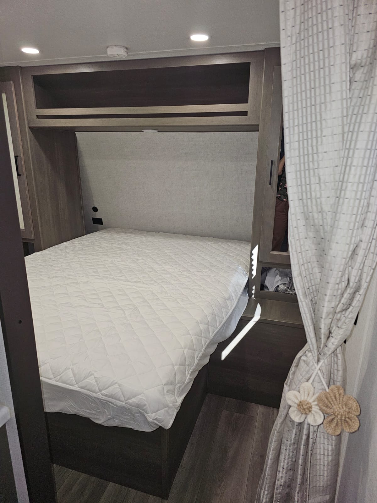 Inside an RV rental: a modern bedroom featuring a neatly made bed, ample overhead storage, and dark wood finishes.. Grand Design Transcend Xplor 2024