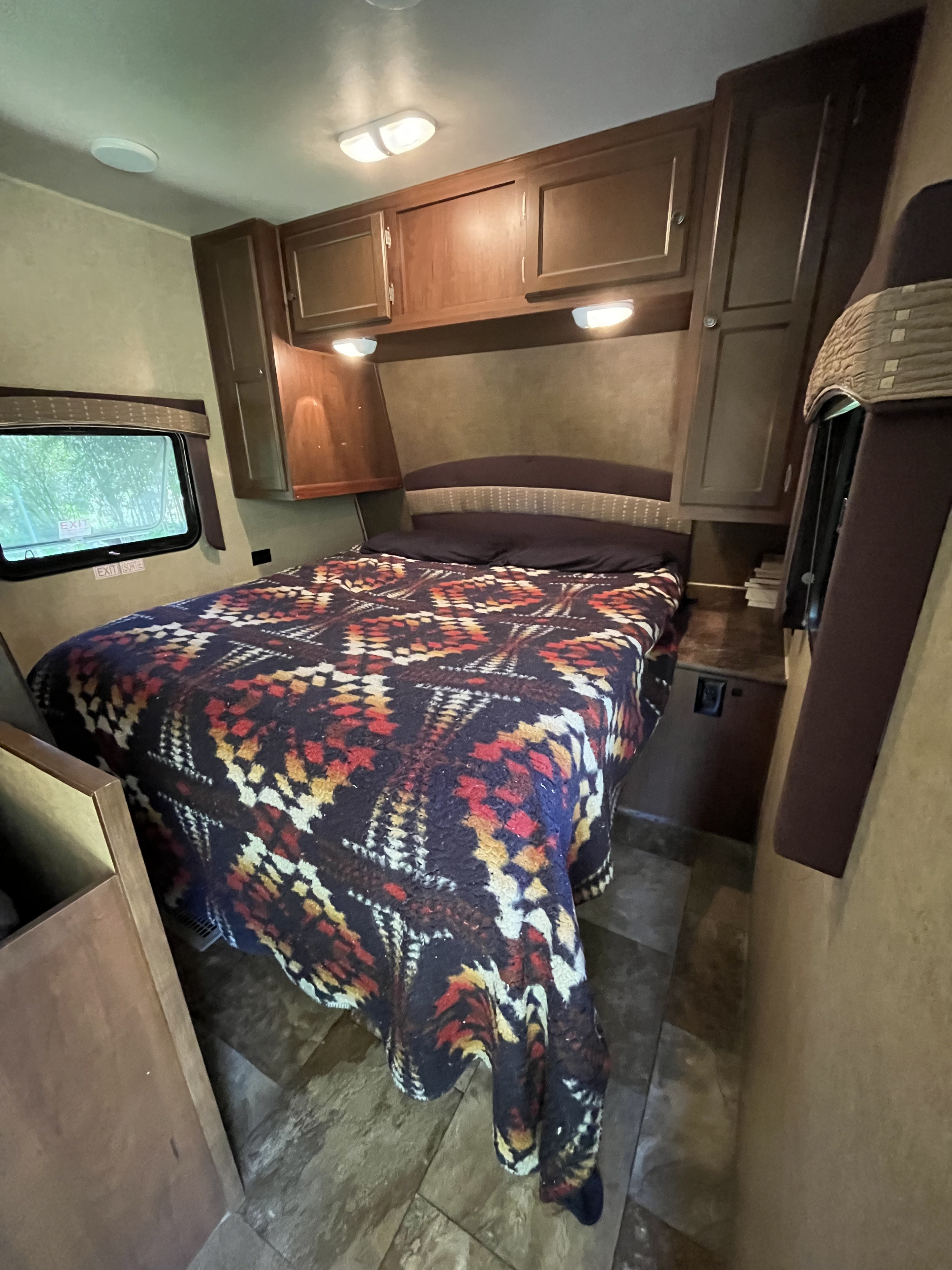 Comfortable RV rental bedroom featuring a colorful patterned bed, overhead cabinets, and an exit window.. Jayco Jay Flight 2014