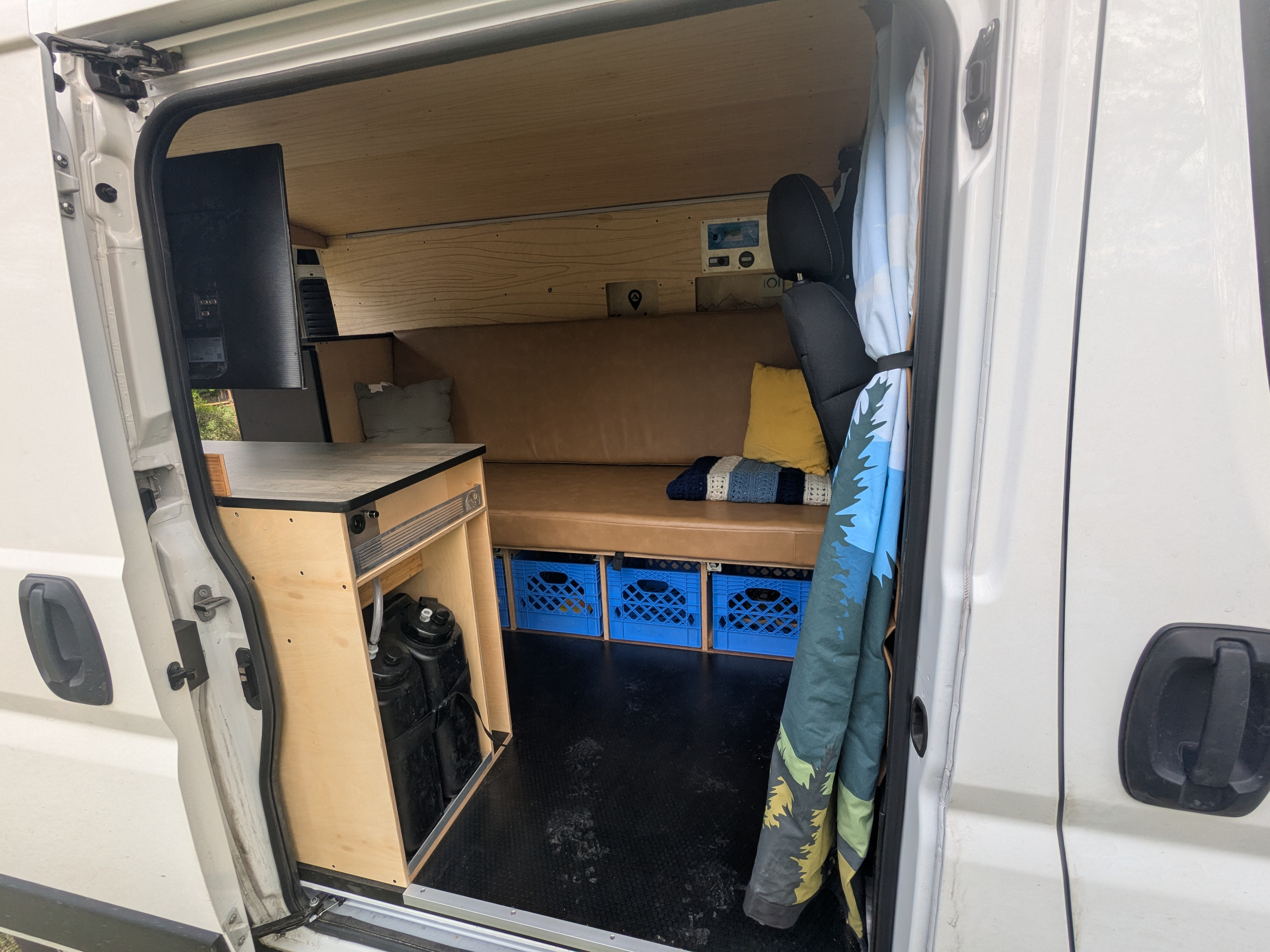 Spacious custom RV rental interior featuring a comfy bench, clever storage with crates, and a full wood build.. RAM Promaster 2023
