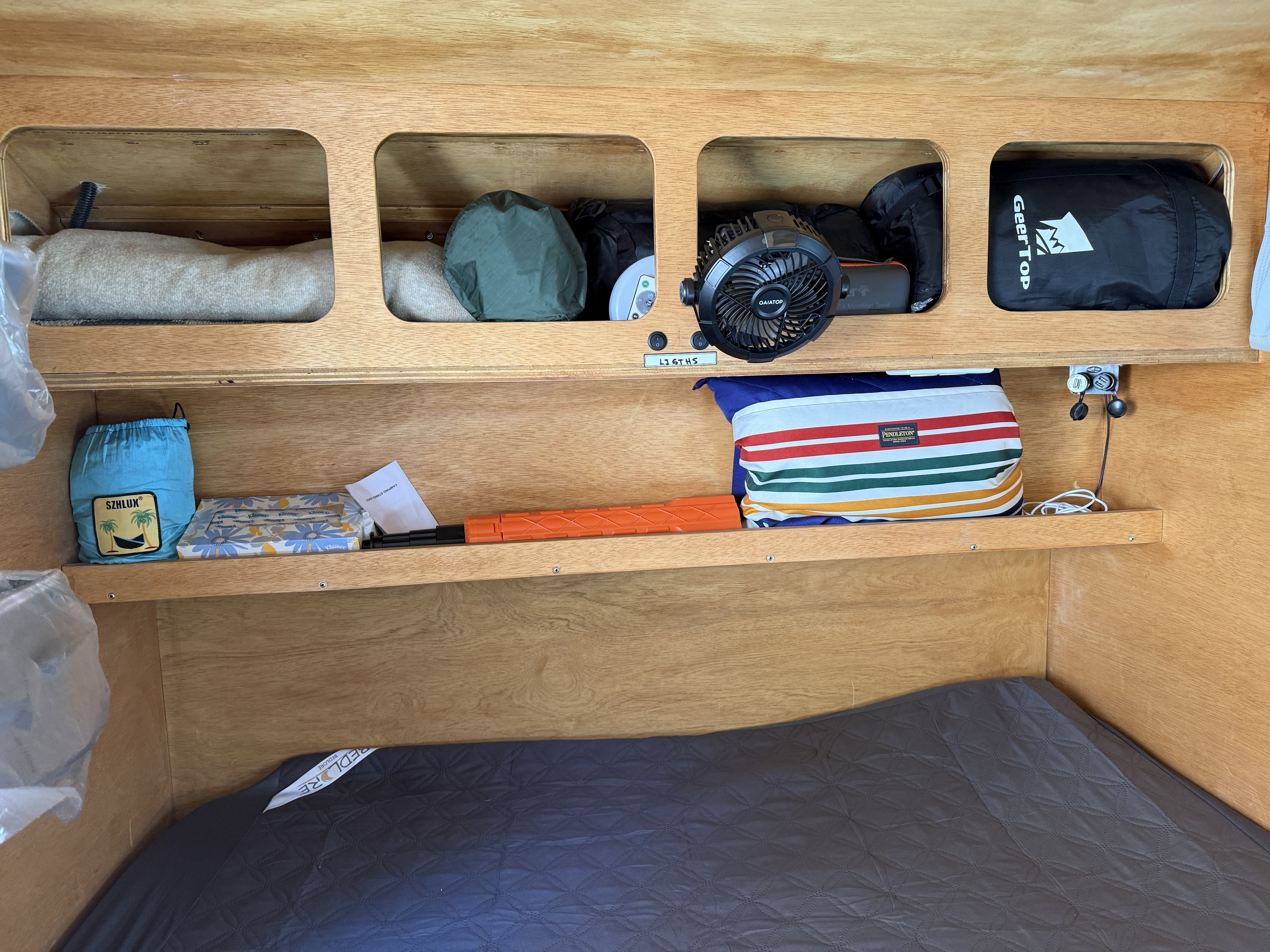 This RV rental's organized interior features built-in wooden shelves, camping gear, fan, and a cozy mattress.. Teardrop Froggy 2021