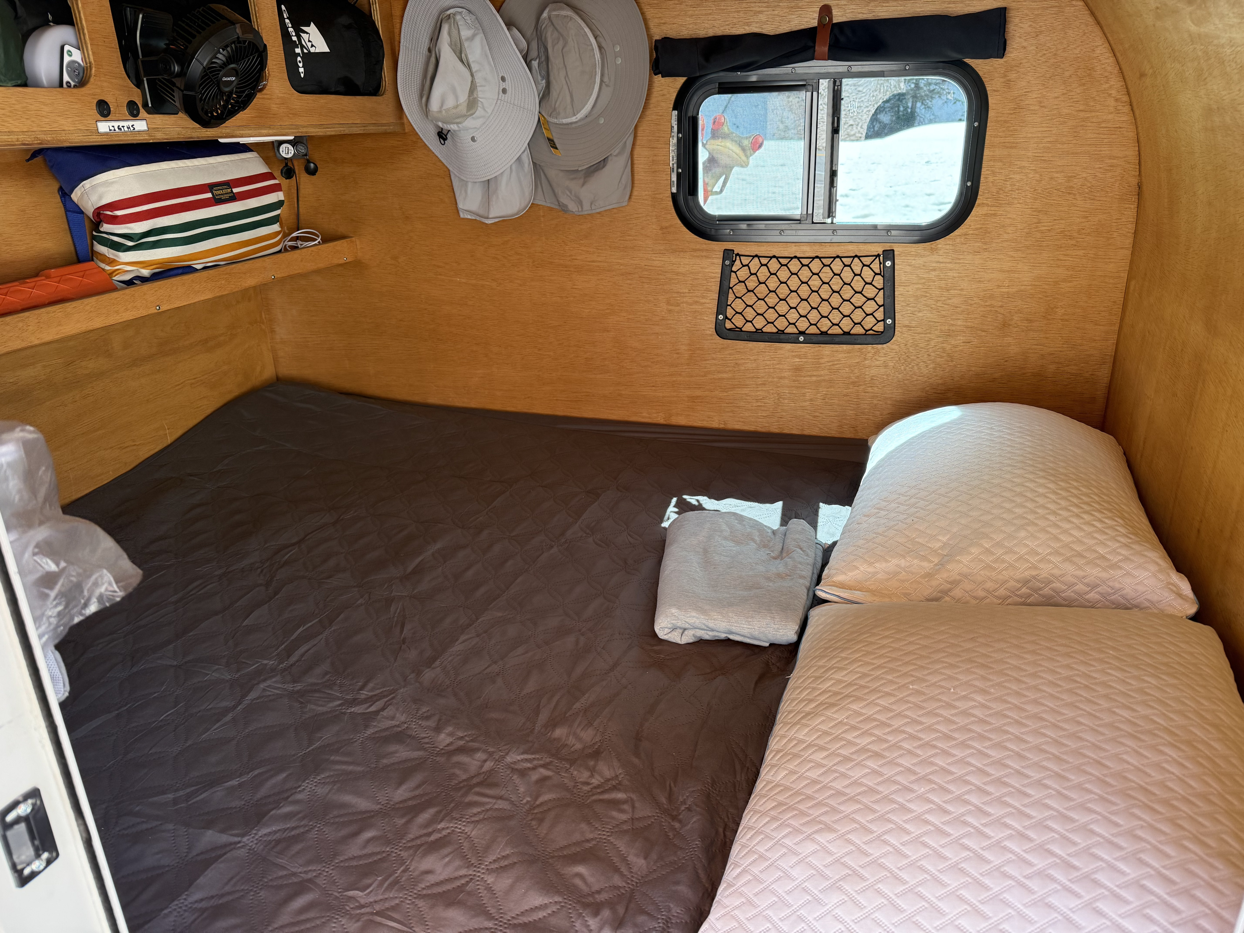 Relax in this RV rental's cozy wooden interior. Features include a comfortable bed, storage, & window with a snowy view.. Teardrop Froggy 2021