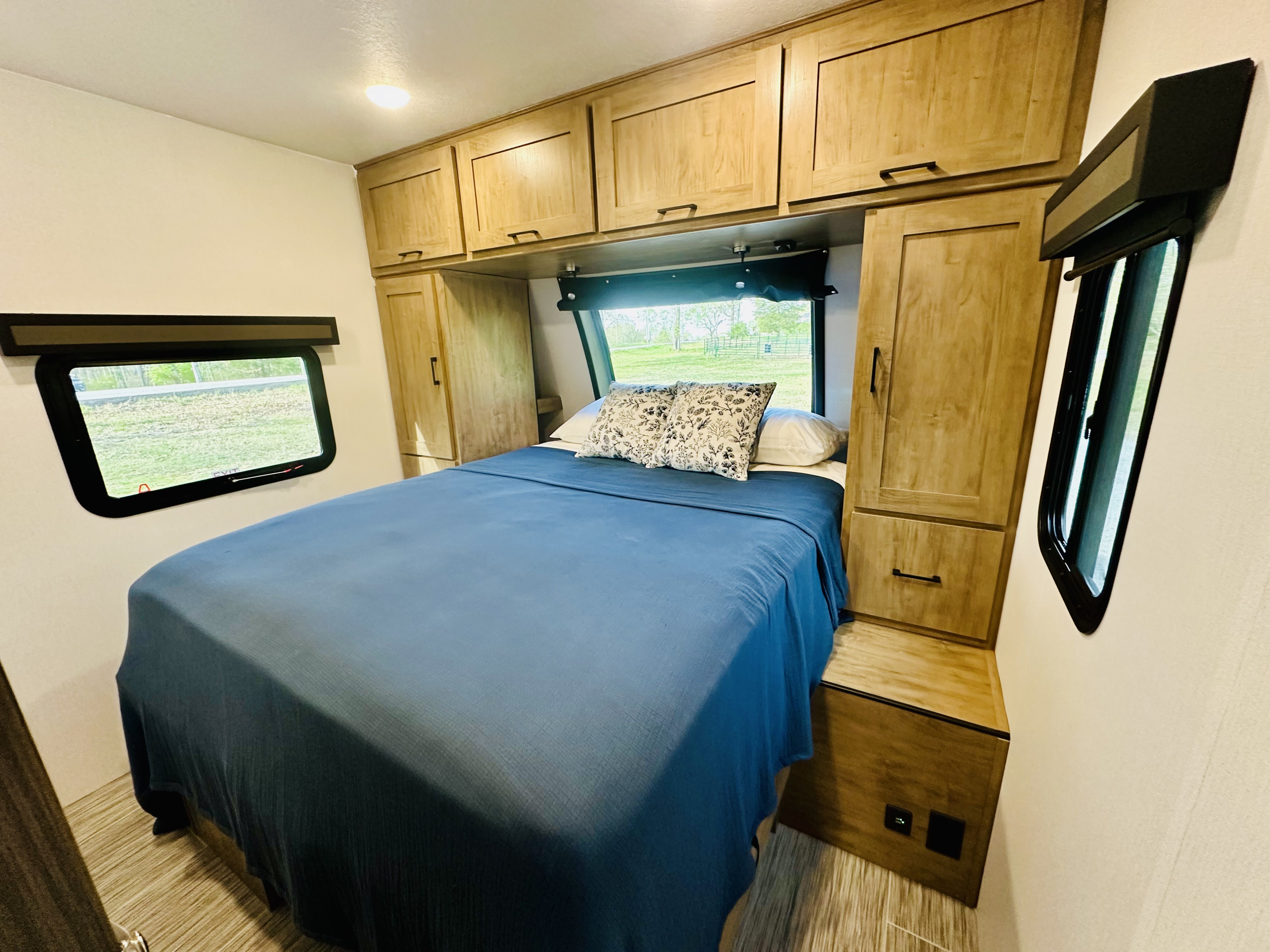 This comfortable RV rental bedroom features a blue bed, ample storage cabinets, and large windows for scenic views.. Forest River Coachmen Freedom Express 2025