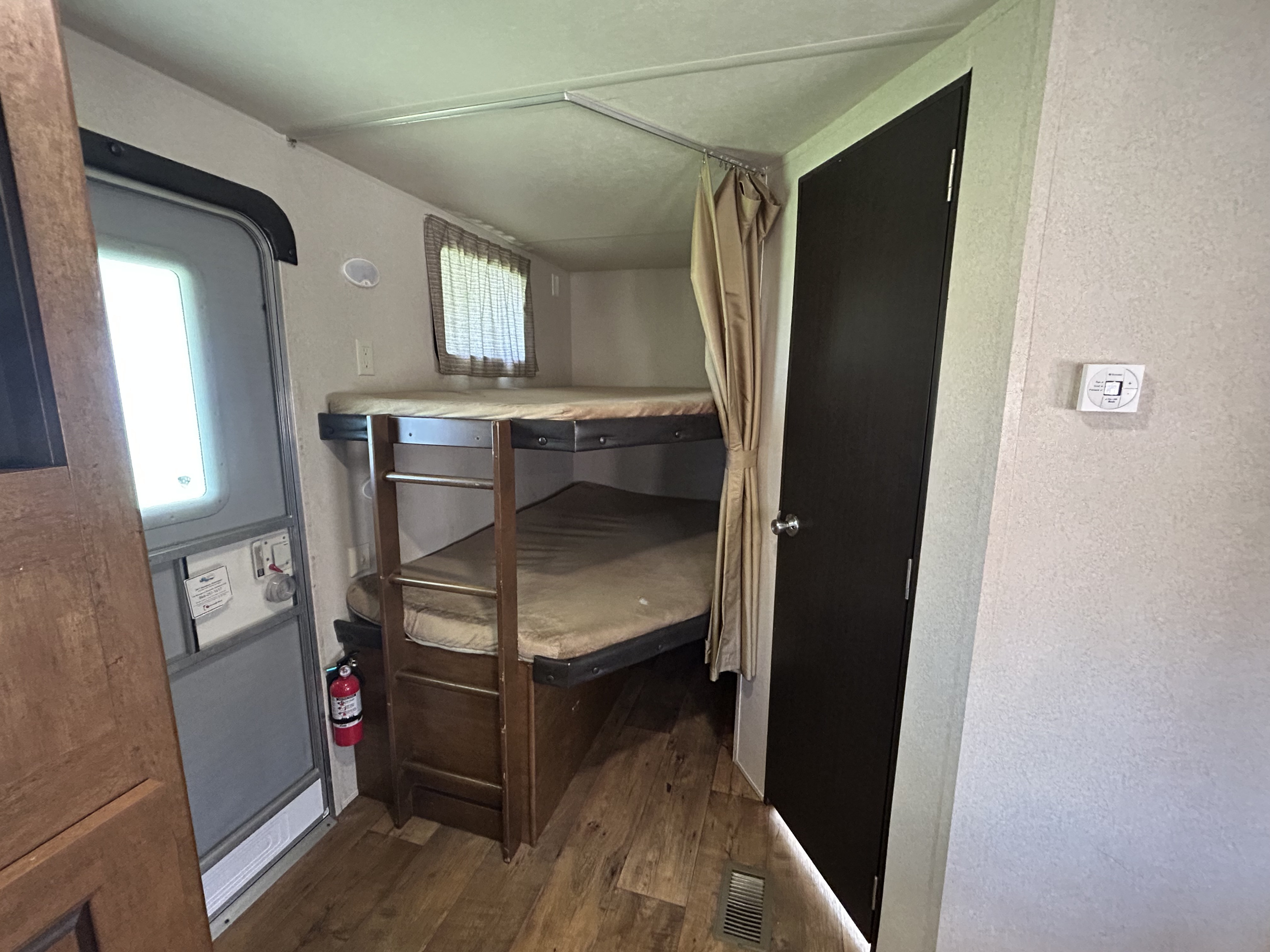 Inside an RV rental, a bunk bed area with two bunks, an entry door, and a fire extinguisher for safety.. Forest River Salem 2017