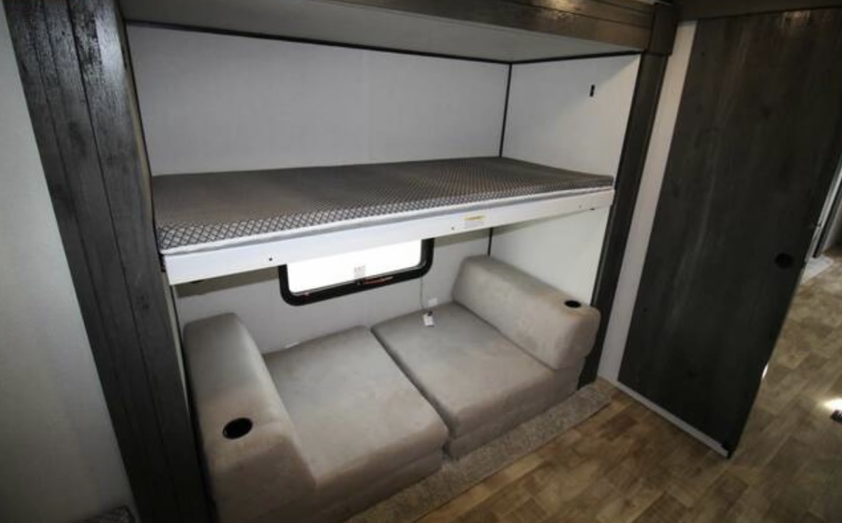 RV rental interior: upper bunk bed over transformable seating with cupholders, ideal for travel.. Keystone RV Hideout 2023