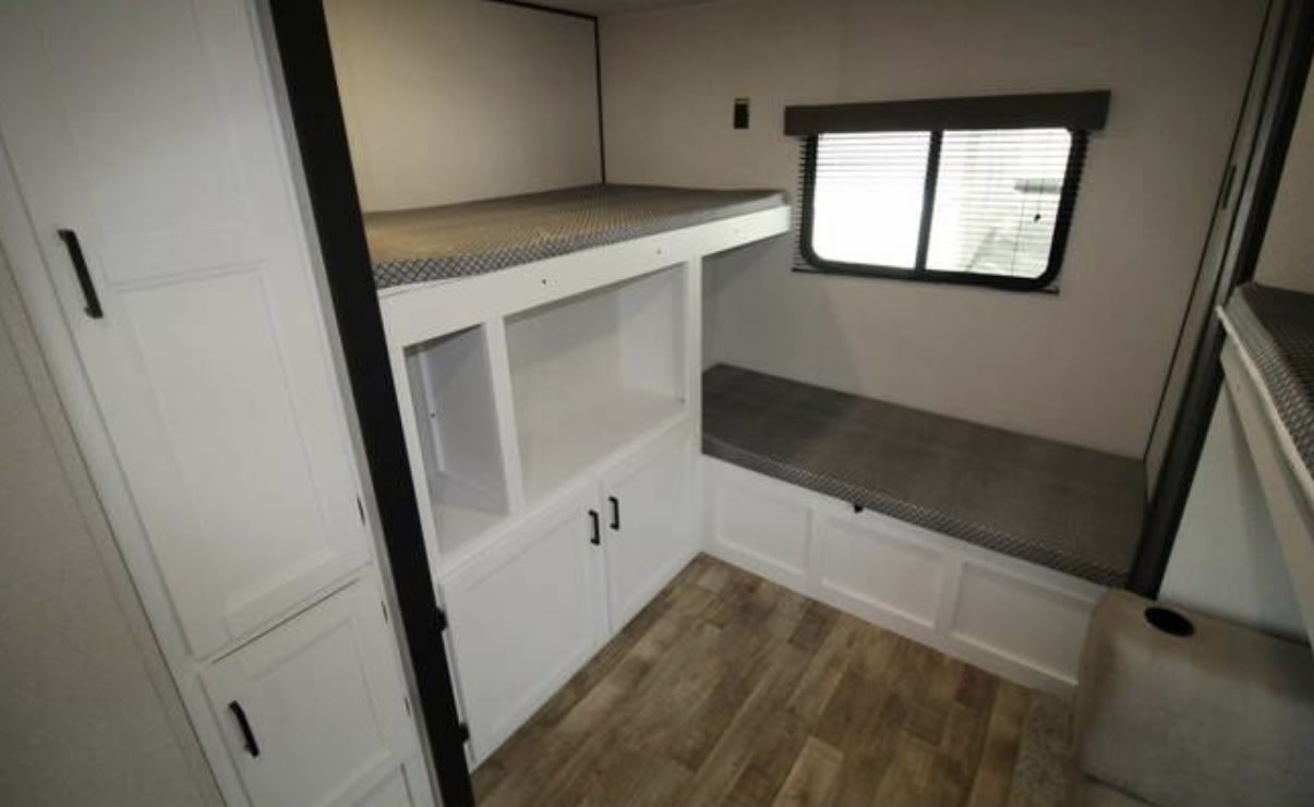 Modern RV rental bunk area features stacked beds, built-in storage, and a comfy bench by the window.. Keystone RV Hideout 2023