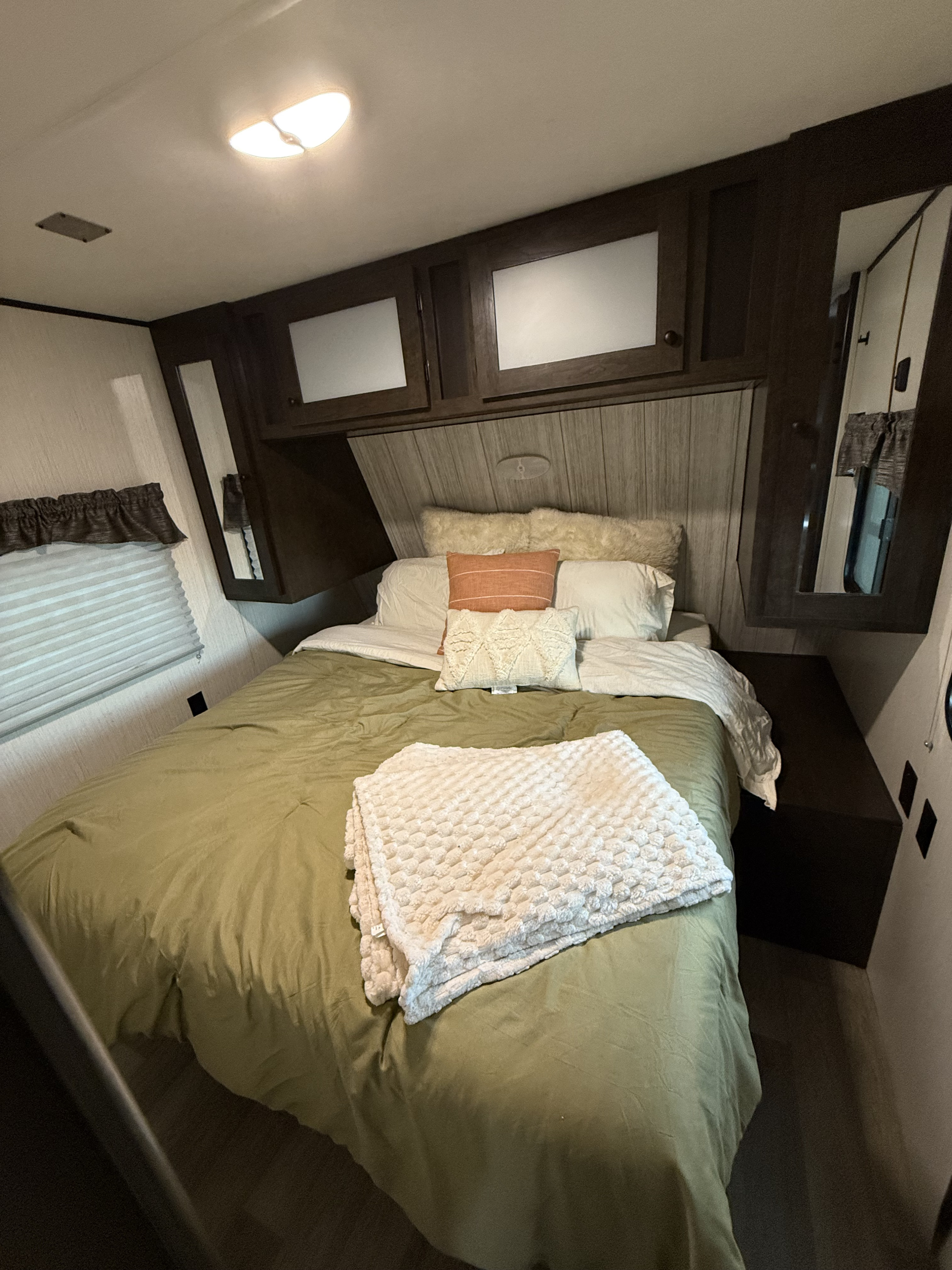 Cozy RV rental bedroom featuring olive green bedding, white pillows, and ample overhead storage for a comfortable stay.. Heartland RVs Pioneer 2022