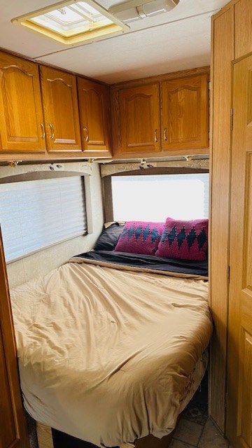 This RV rental bedroom features a cozy bed, wooden overhead cabinets, and windows with blinds.. Forest River Sunseeker 2001