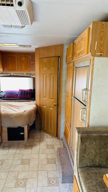 RV rental: Bedroom with cozy bed, wood cabinets, fridge, and dinette. Tiled floor, AC unit visible.. Forest River Sunseeker 2001