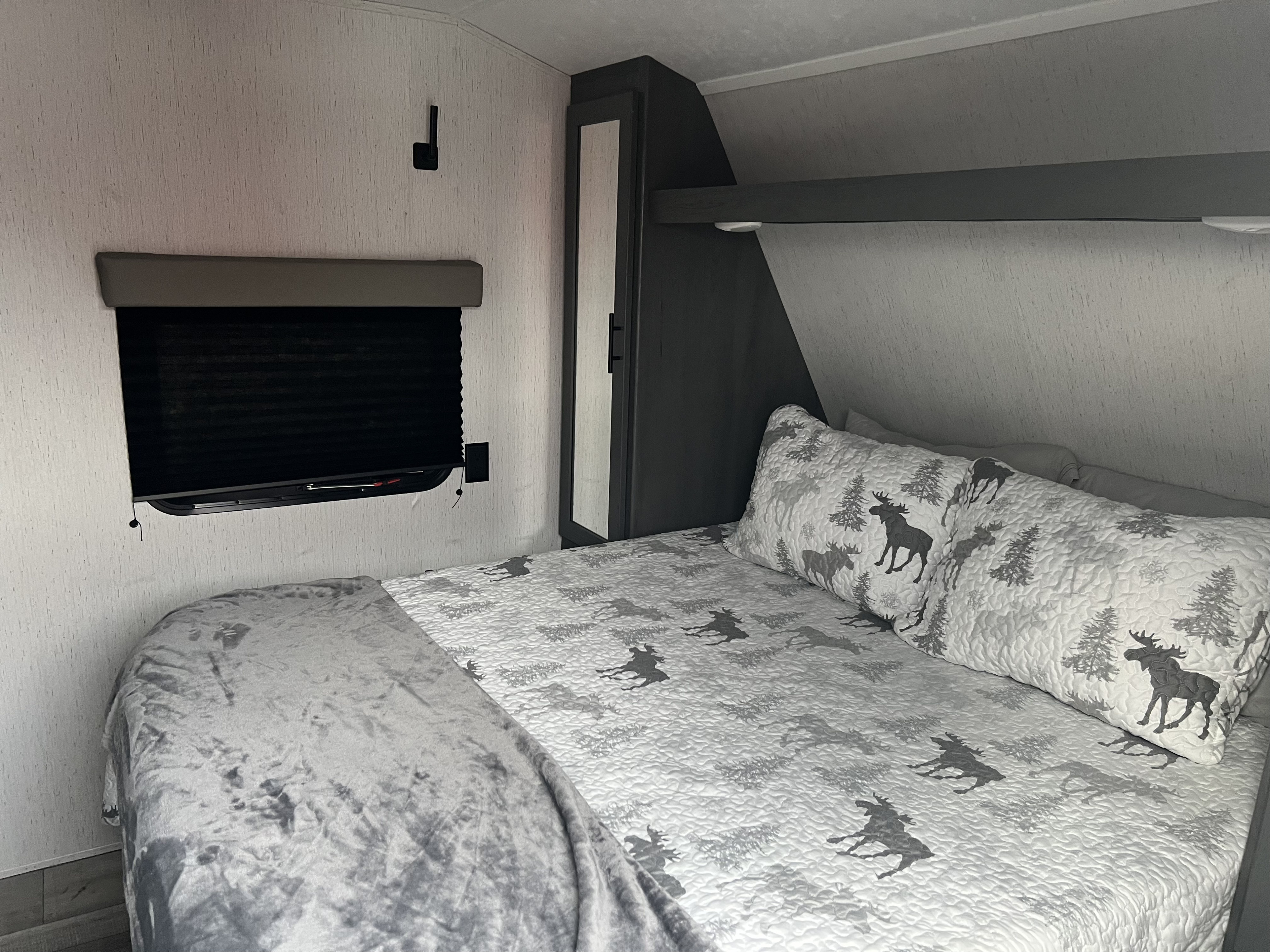 Cozy RV rental bedroom with a bed, window, and storage, featuring moose and tree themed bedding.. Aspen Trail Aspen Trail Trailer 2021