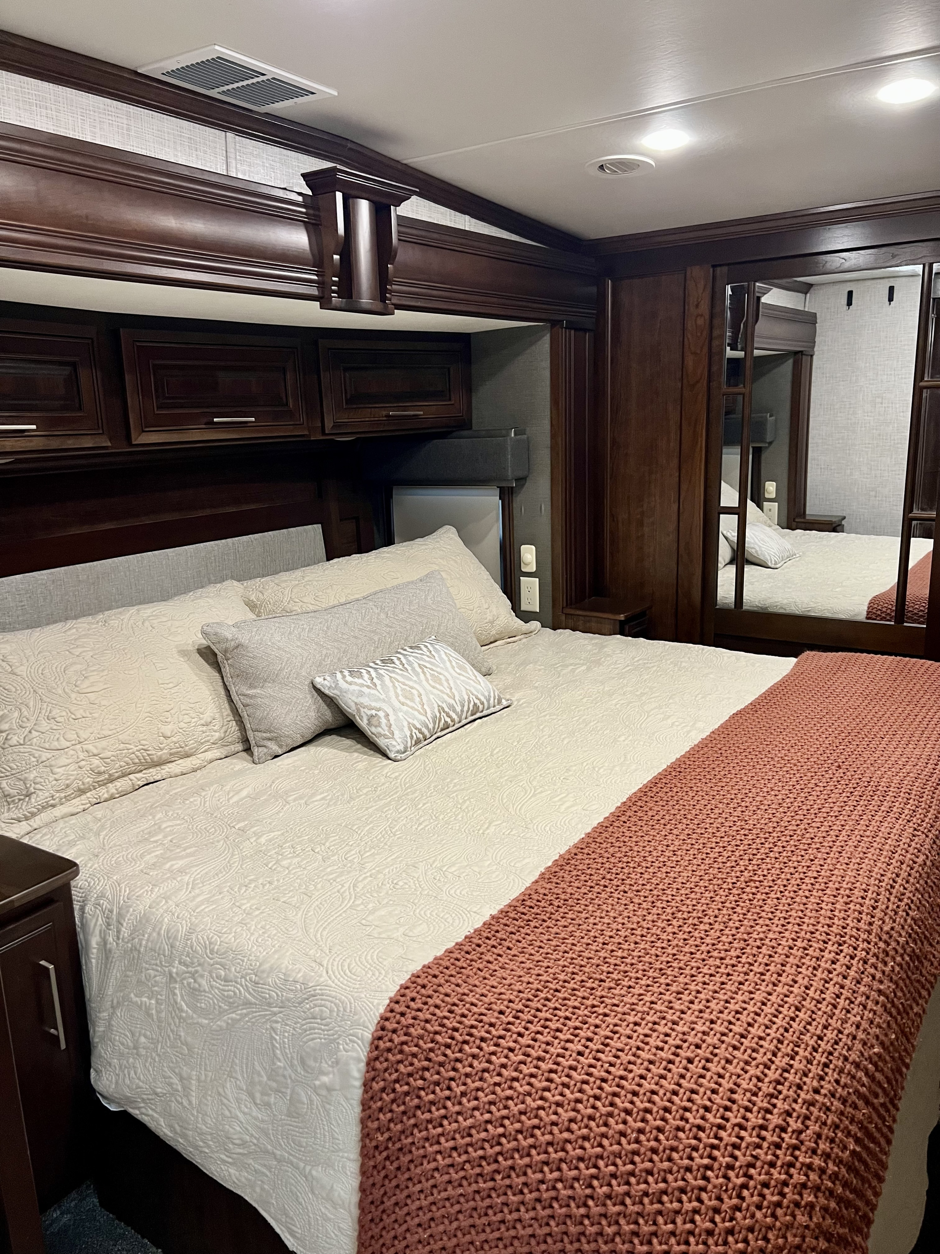Explore this luxurious RV rental bedroom: large bed with light quilted bedding, orange throw, rich wood cabinets & mirrored wardrobe.. Drv Fullhouse LX455 2019