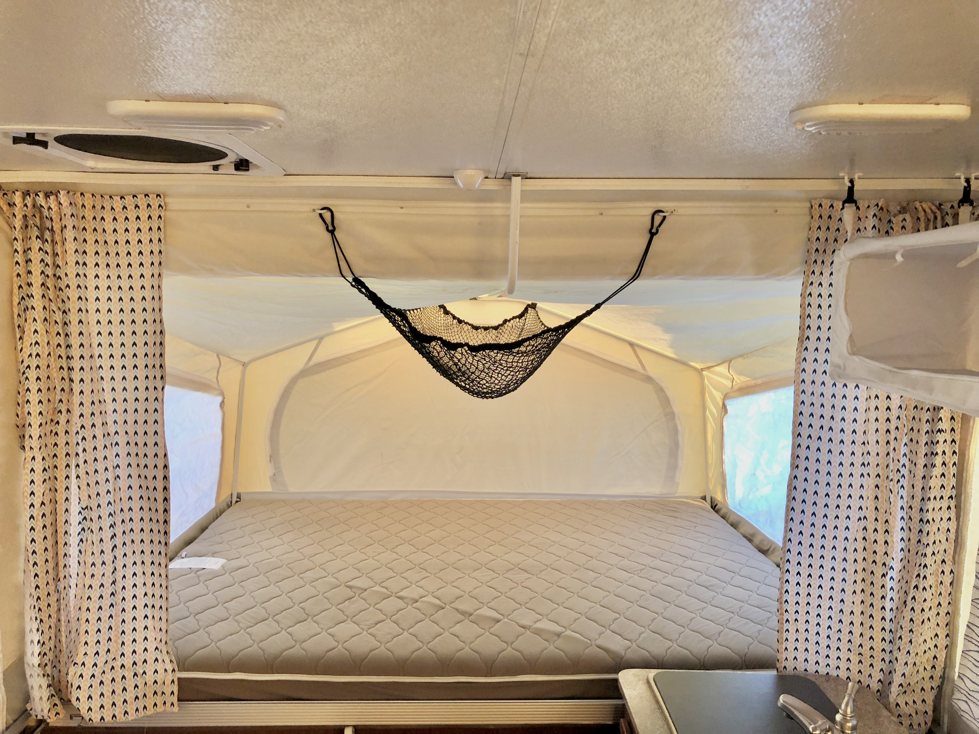 RV rental pop-up camper interior. Features a comfy bed, storage net, and patterned curtains.. Forest River Rockwood Premier 2016