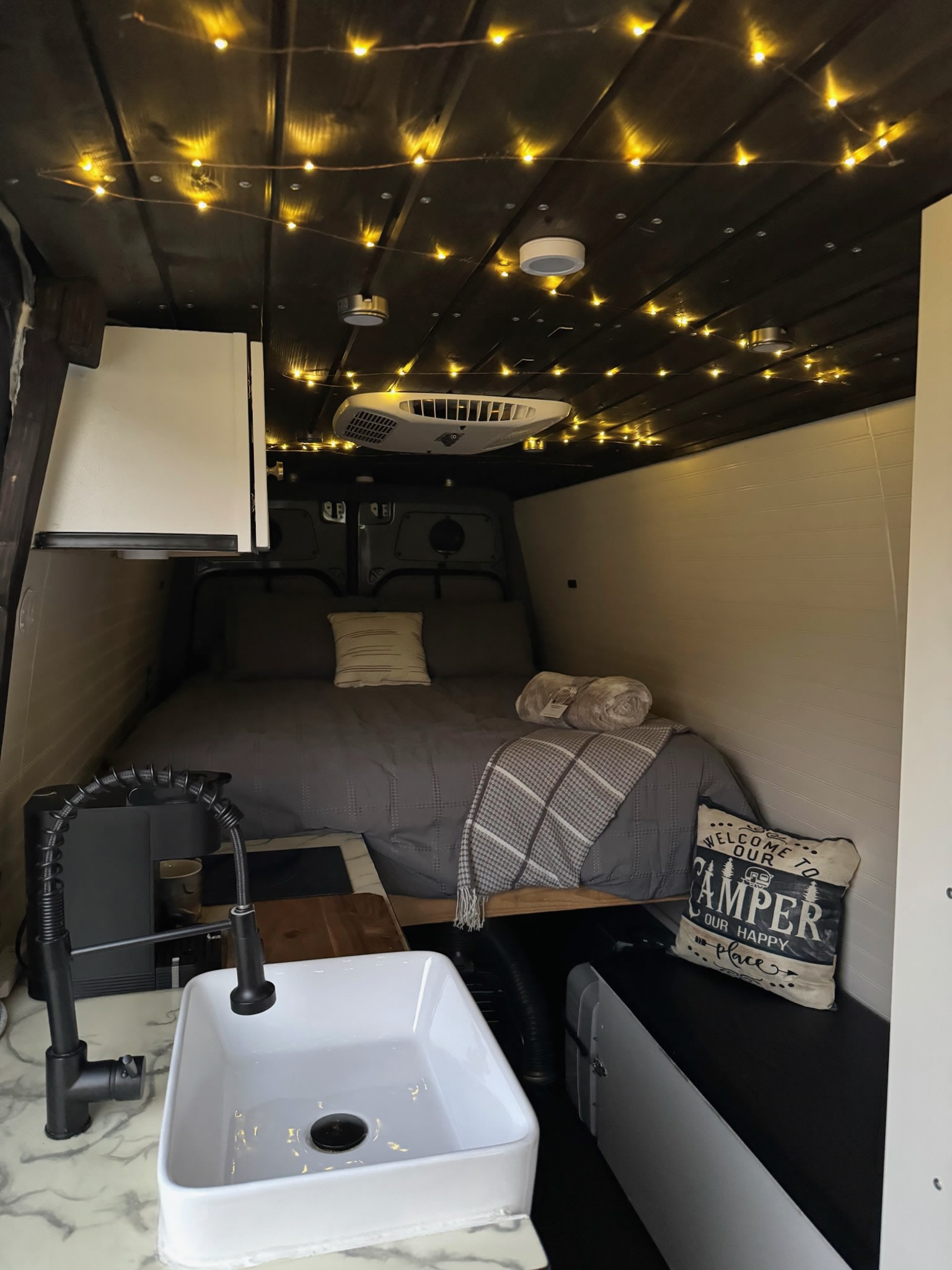 Step inside this cozy rv rental van! Enjoy the inviting bed, warm string lights, and functional kitchen with sink & faucet.. Mercedes-Benz Sprinter 2017