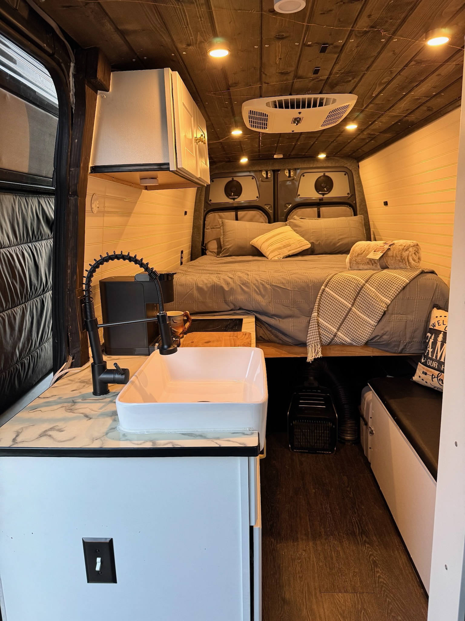 Cozy RV rental interior with bed, kitchen, and wood ceiling. Perfect for compact living on the road.. Mercedes-Benz Sprinter 2017