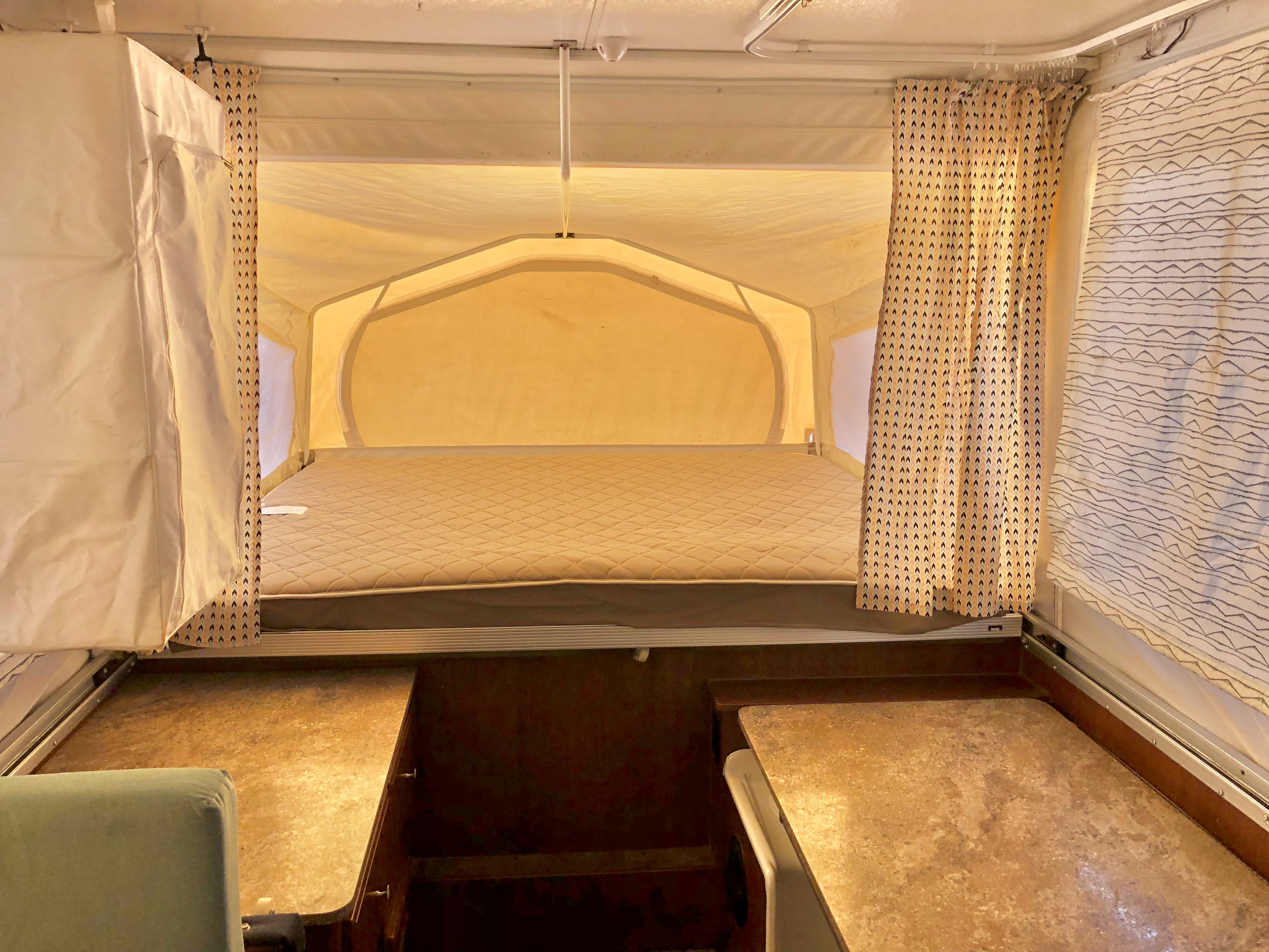 RV rental pop-up: View of the comfy, quilted bed inside the canvas extension, flanked by patterned curtains.. Forest River Rockwood Premier 2016