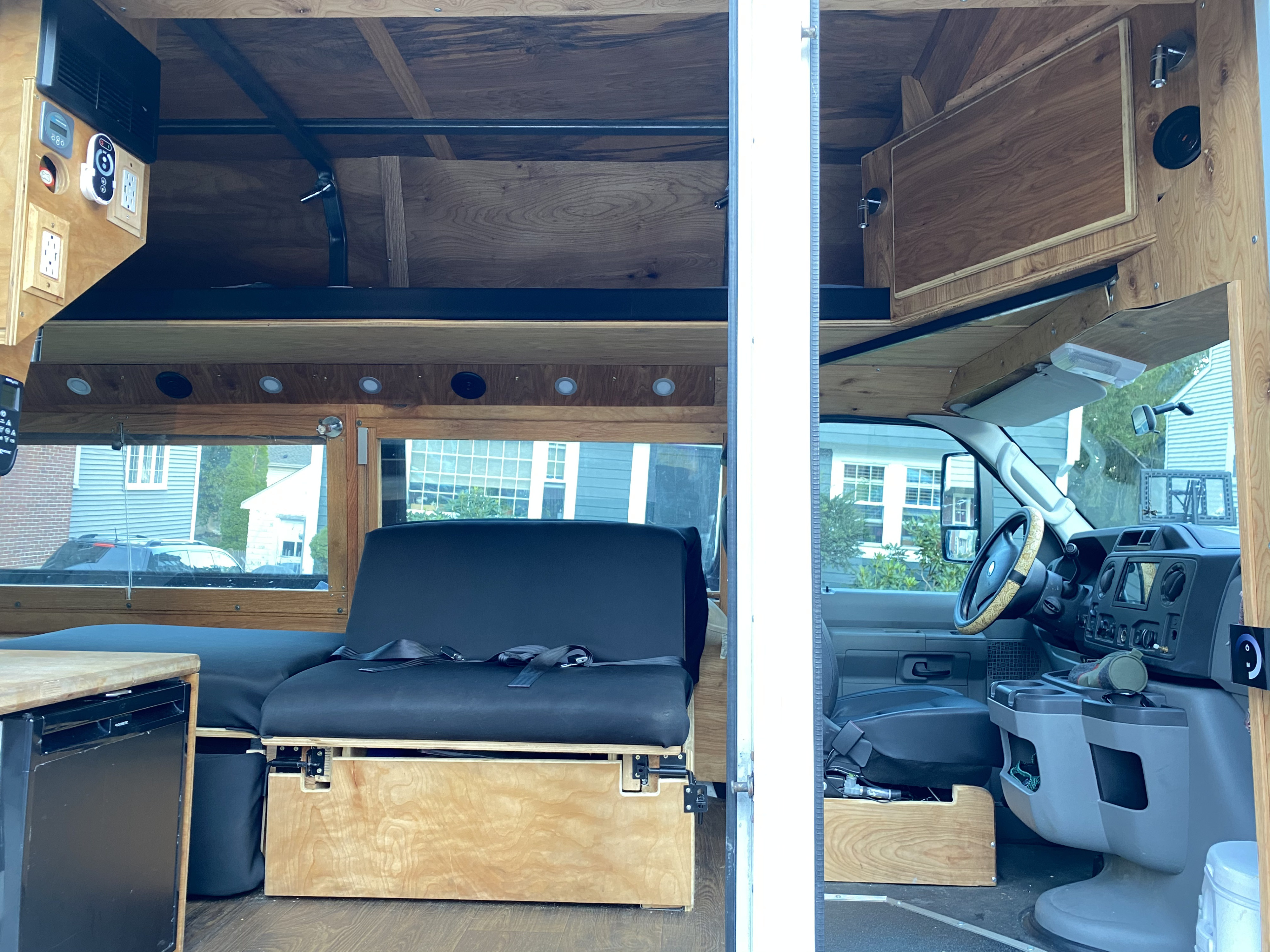 Custom-built RV rental camper van interior featuring wooden cabinetry, convertible seating, a compact fridge, and overhead bed platform.. Ford Econoline 2011