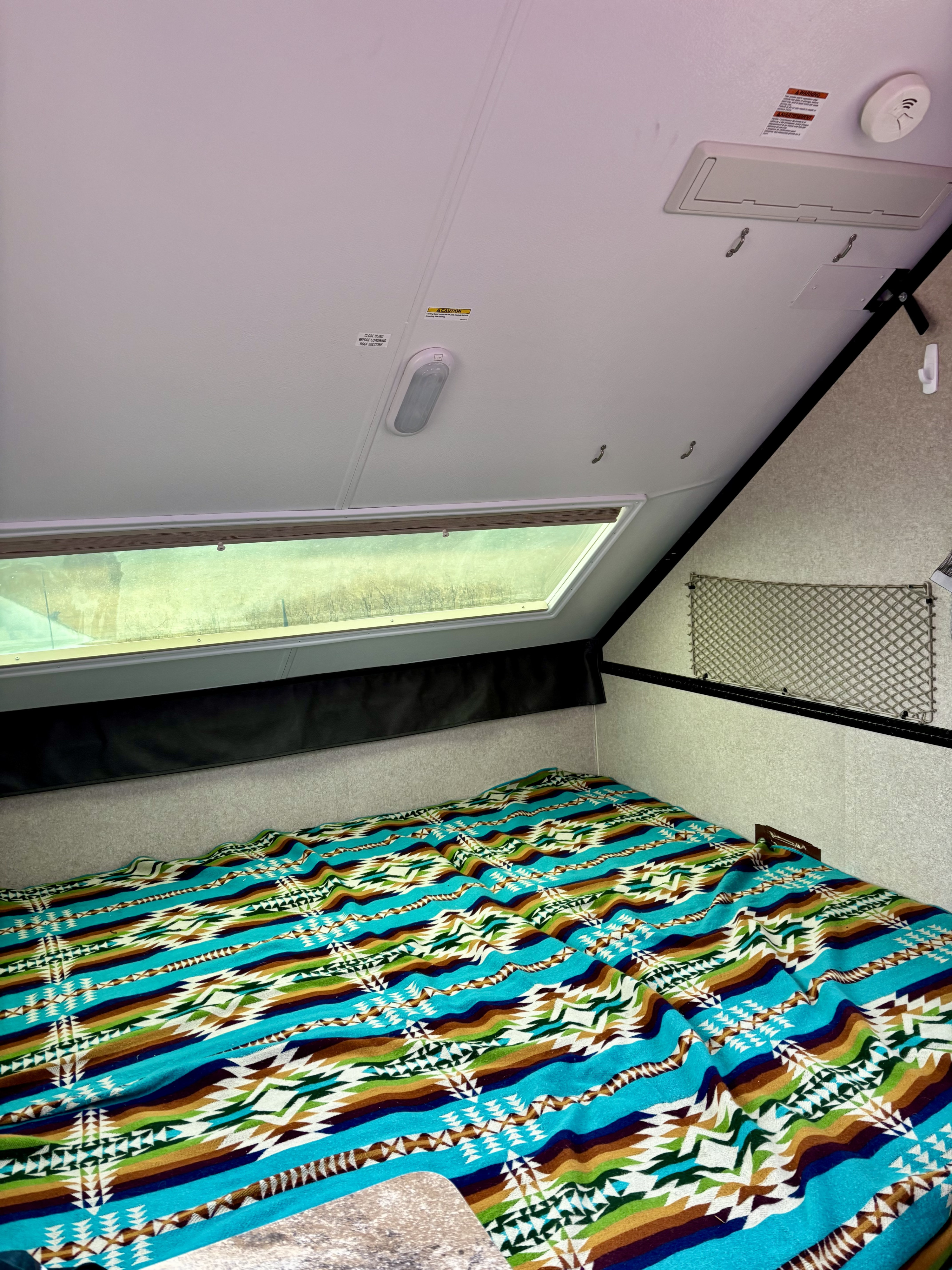 Cozy RV rental interior: Vibrant patterned blanket on bed, large skylight. Ceiling has light & smoke detector.. Forest River Rockwood Premier 2019