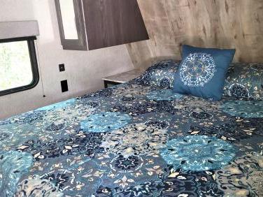 Inside an RV rental: a bright bedroom with blue patterned bedding, wall-mounted cabinet, and window view.. Dutchmen Guide 2027RD 2020