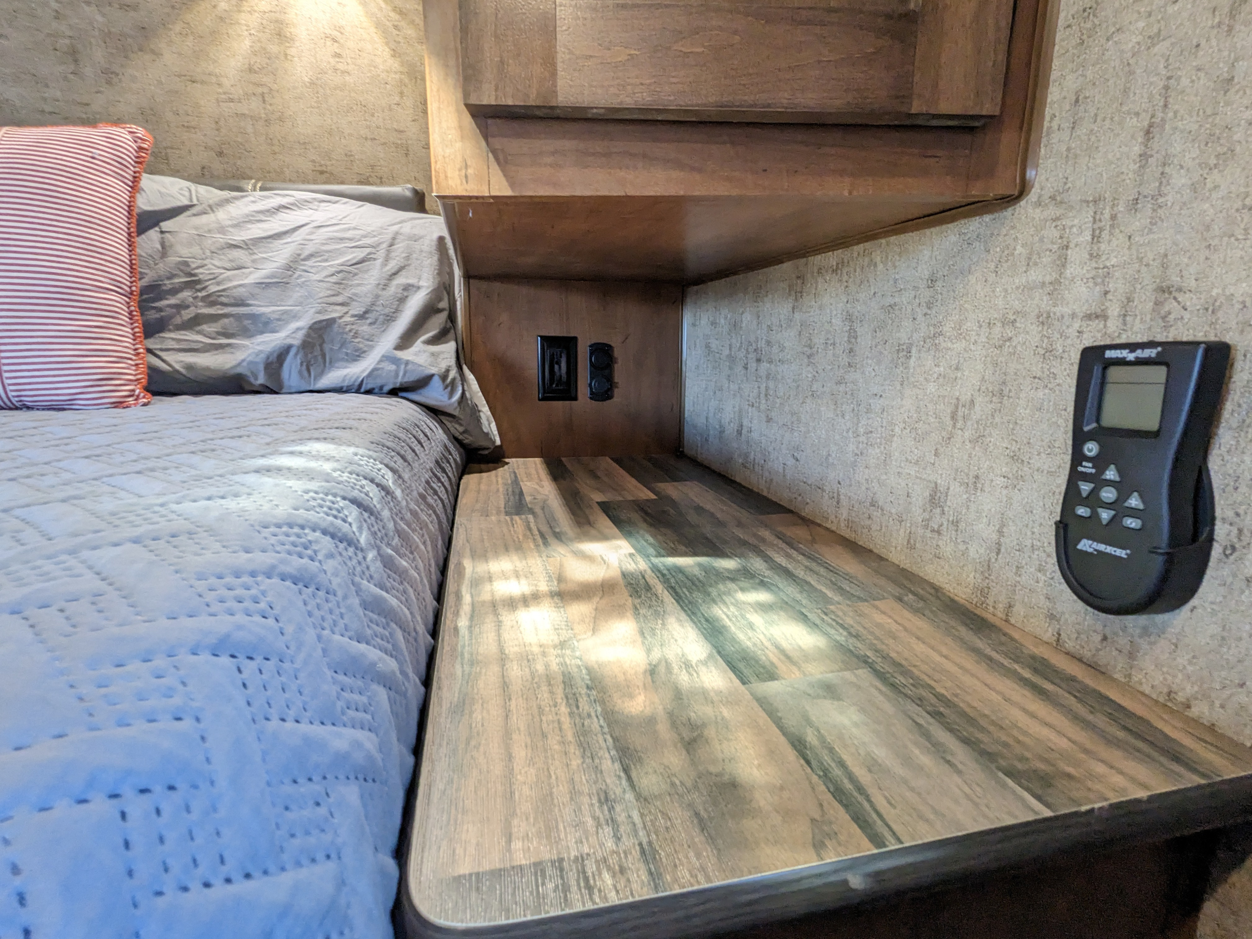 RV rental bedroom: a cozy bed next to a compact wood-look nightstand with outlets and a mounted climate control remote.. Outdoors RV Timber Ridge 2022