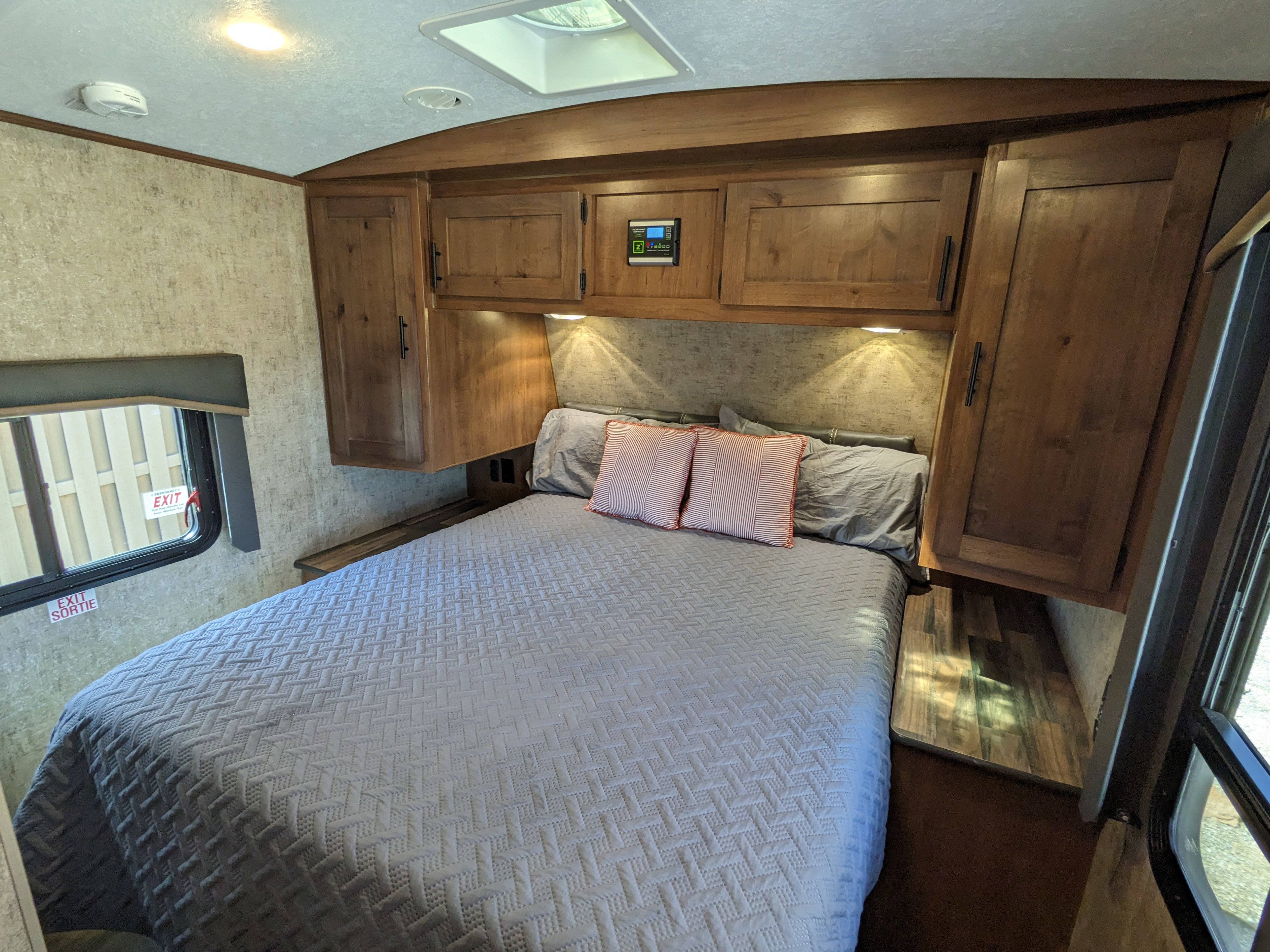 Cozy RV rental bedroom featuring a comfy bed, overhead cabinets, and emergency exit window for your next adventure.. Outdoors RV Timber Ridge 2022
