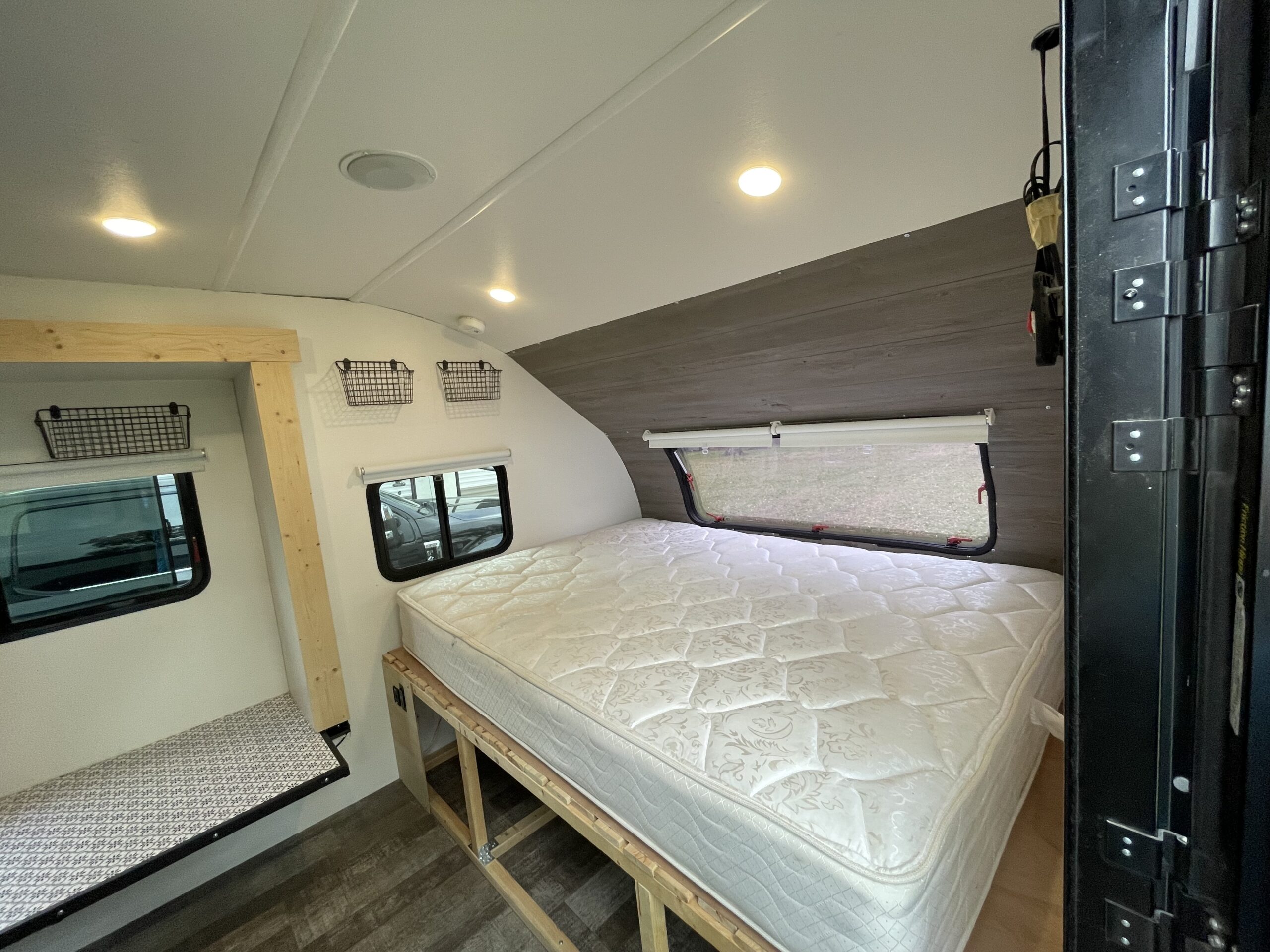 Inviting RV rental interior: a comfy bedroom with a quilted mattress, windows, bright lights, and wire storage baskets.. Forest River R Pod 2022