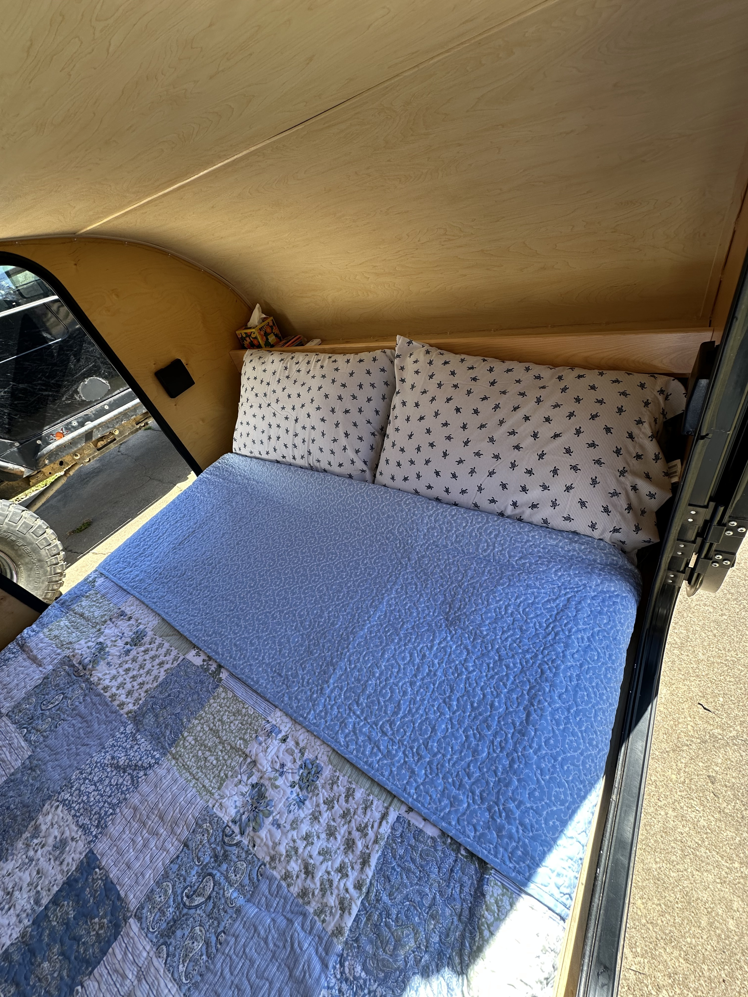 Cozy RV rental interior: a comfy bed with patterned pillows and quilts, set against light wood paneling.. Little Guy Little Guy Trailer 2012