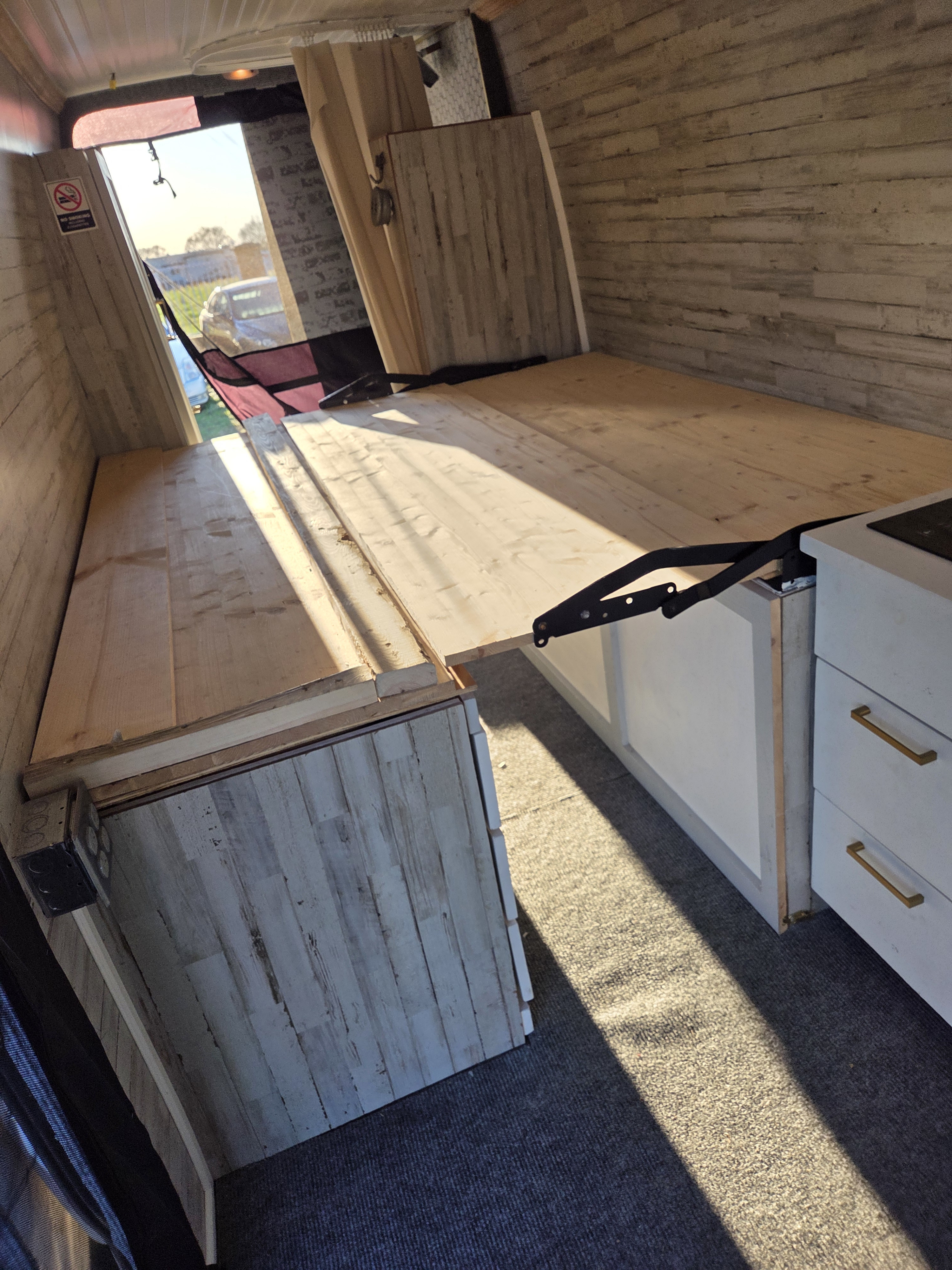 RV rental interior: custom wood bed, paneled walls, and compact kitchen. Sunlight illuminates the cozy, adventure-ready space.. Mercedes-Benz Sprinter 2018