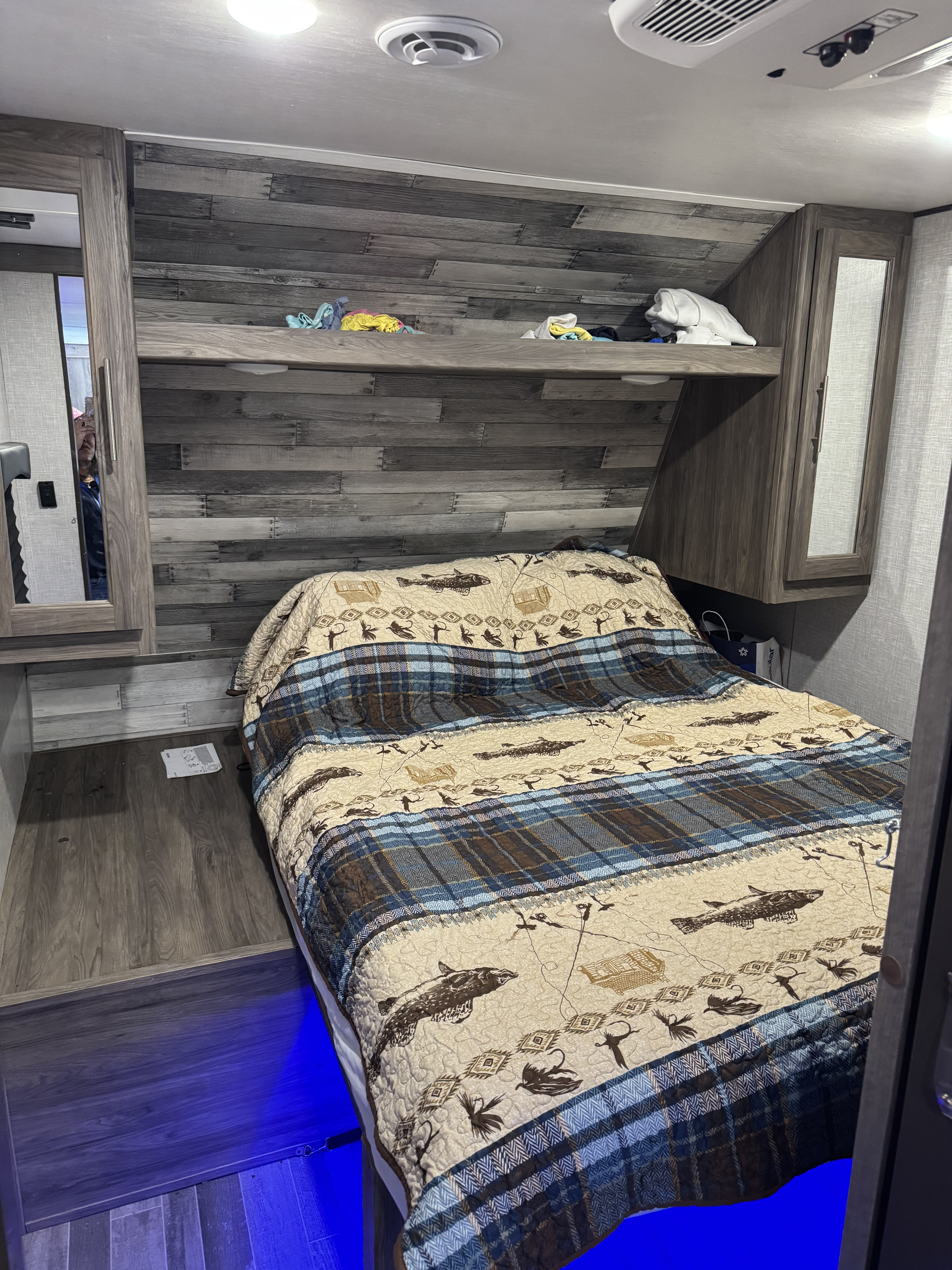 Cozy RV rental bedroom features a bed with fish & plaid quilt, overhead storage, and vibrant blue under-bed lighting.. Crossroads RV Zinger 2022