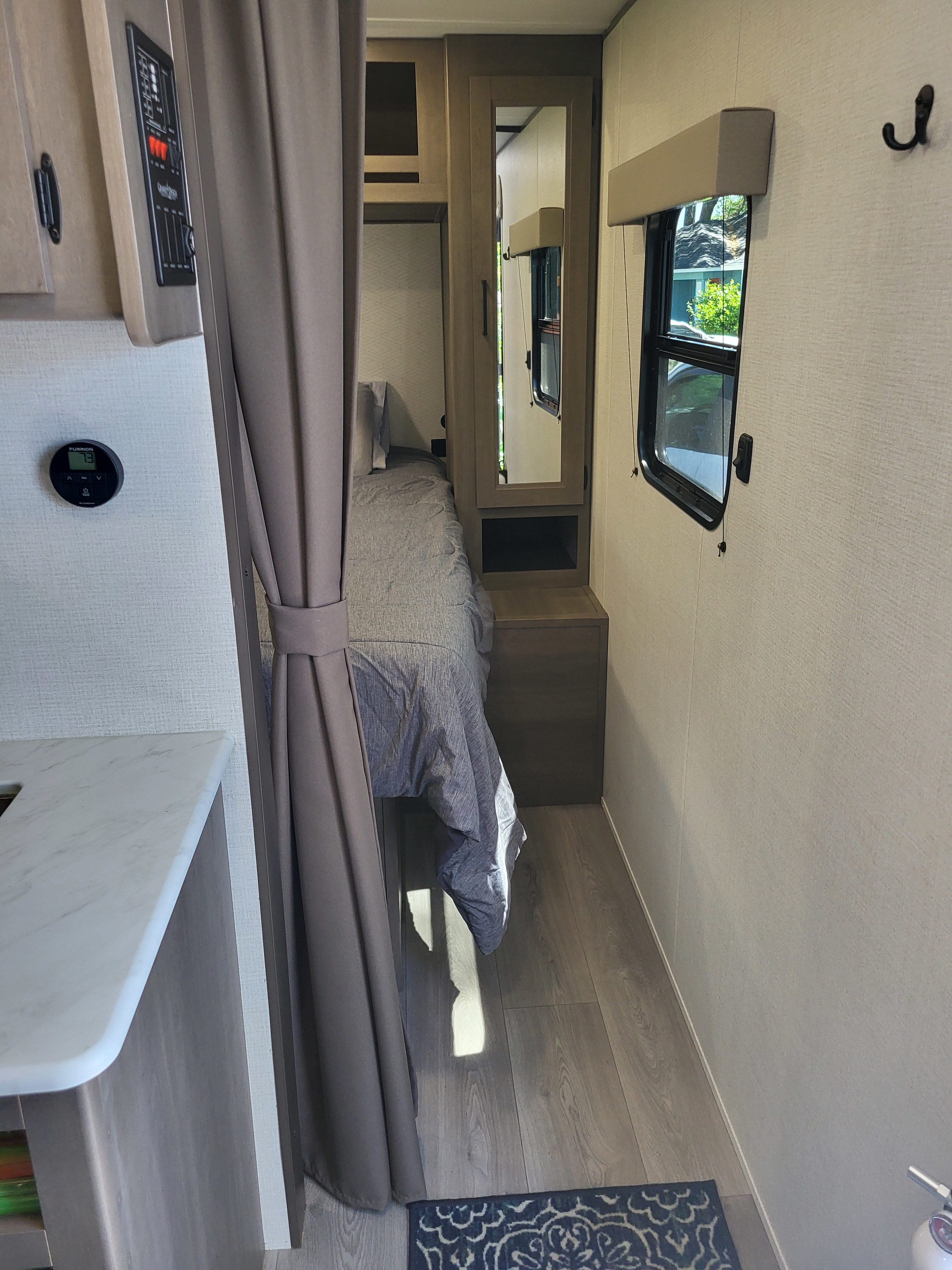 Cozy RV rental bedroom area featuring a comfortable bed, mirrored closet, tank control panel, and thermostat.. Grand Design Transcend Xplor 24BHX 2025