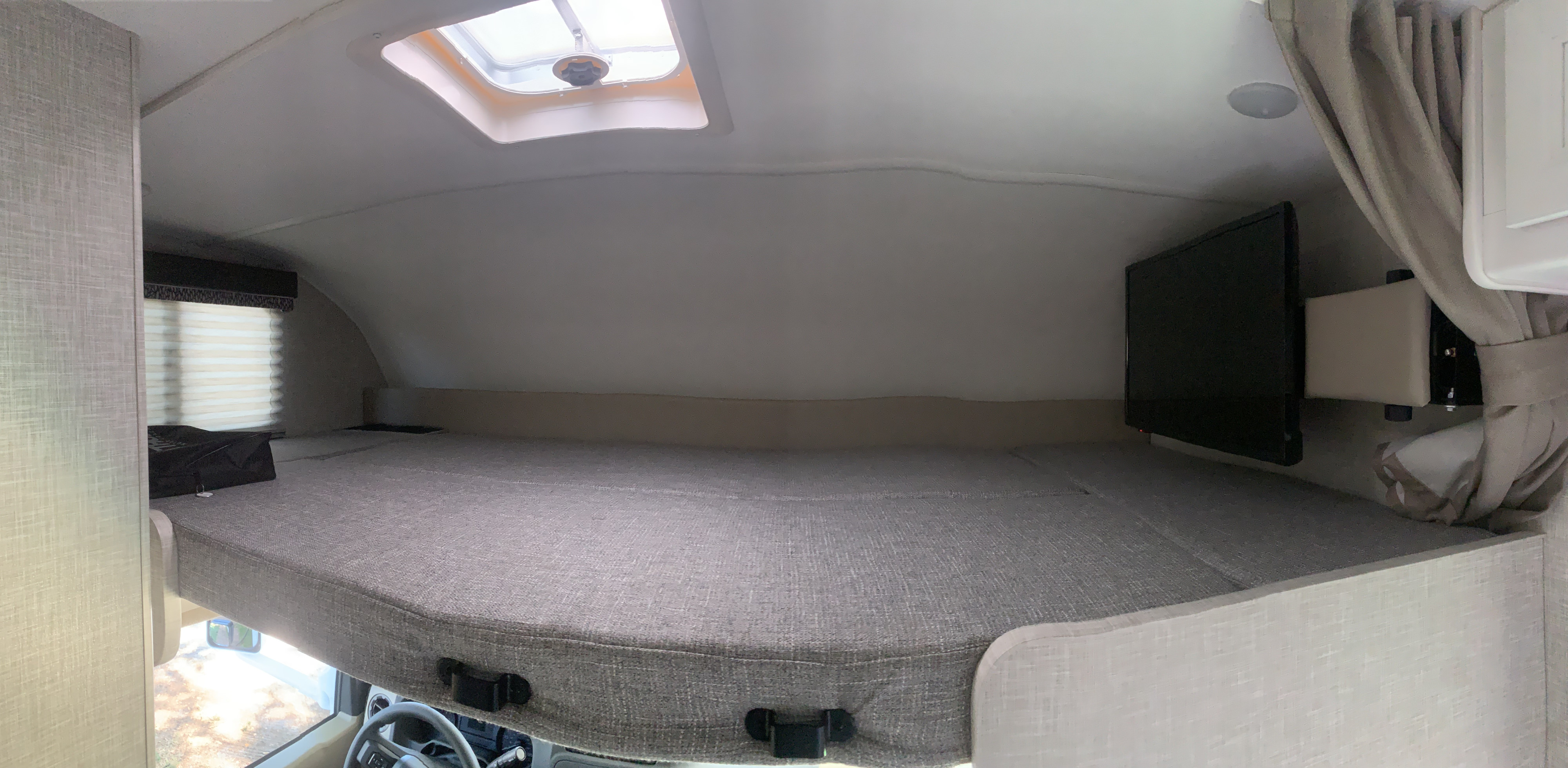 Discover the comfy cab-over bunk of this RV rental, with a soft bed, mounted TV, window, and skylight above.. THOR THOR QUANTUM LC19 2025