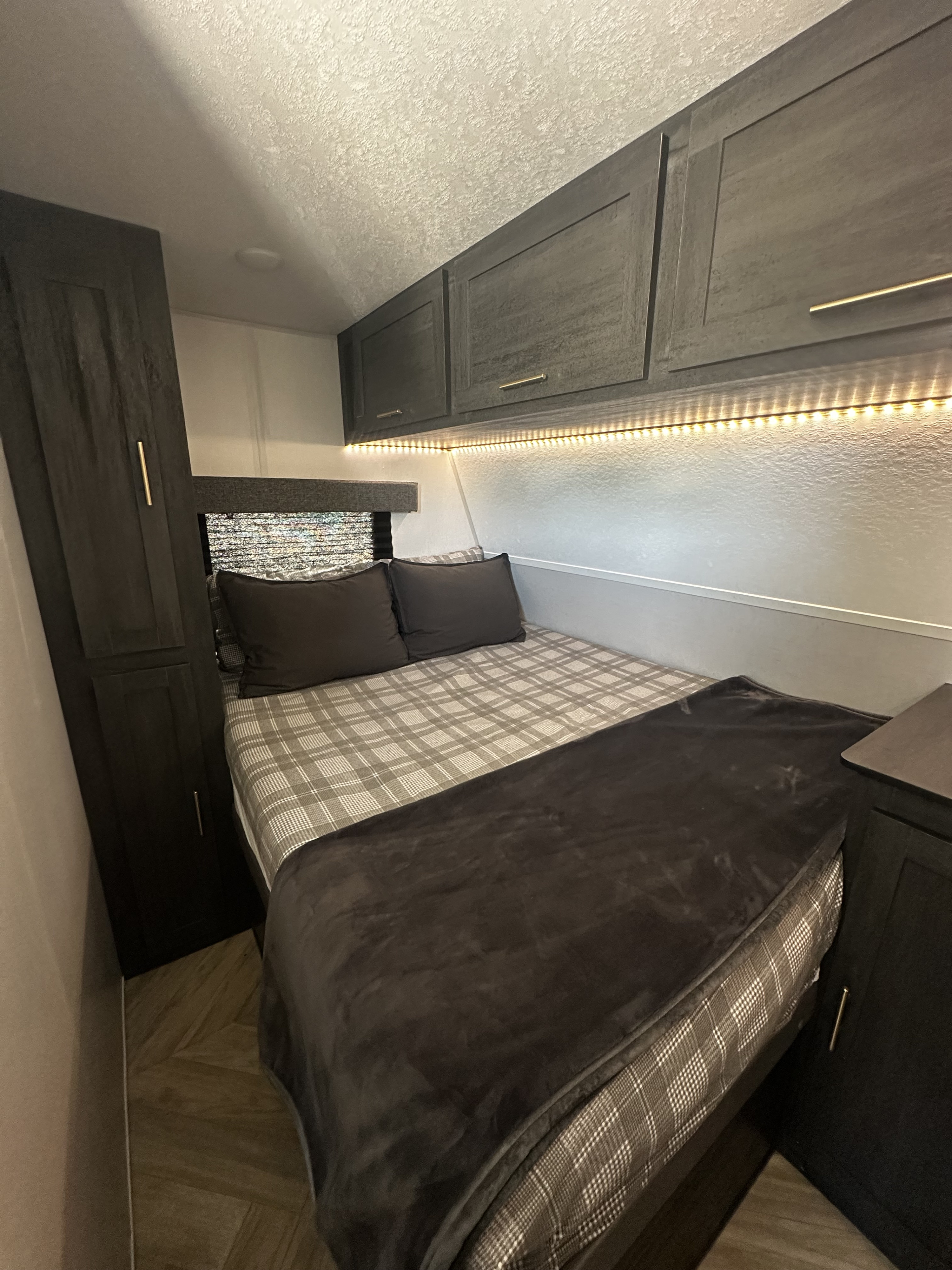 Cozy RV rental bedroom featuring a plaid bed, dark cabinets with LED lighting, and wood-look flooring.. Forest River Ozark 2022
