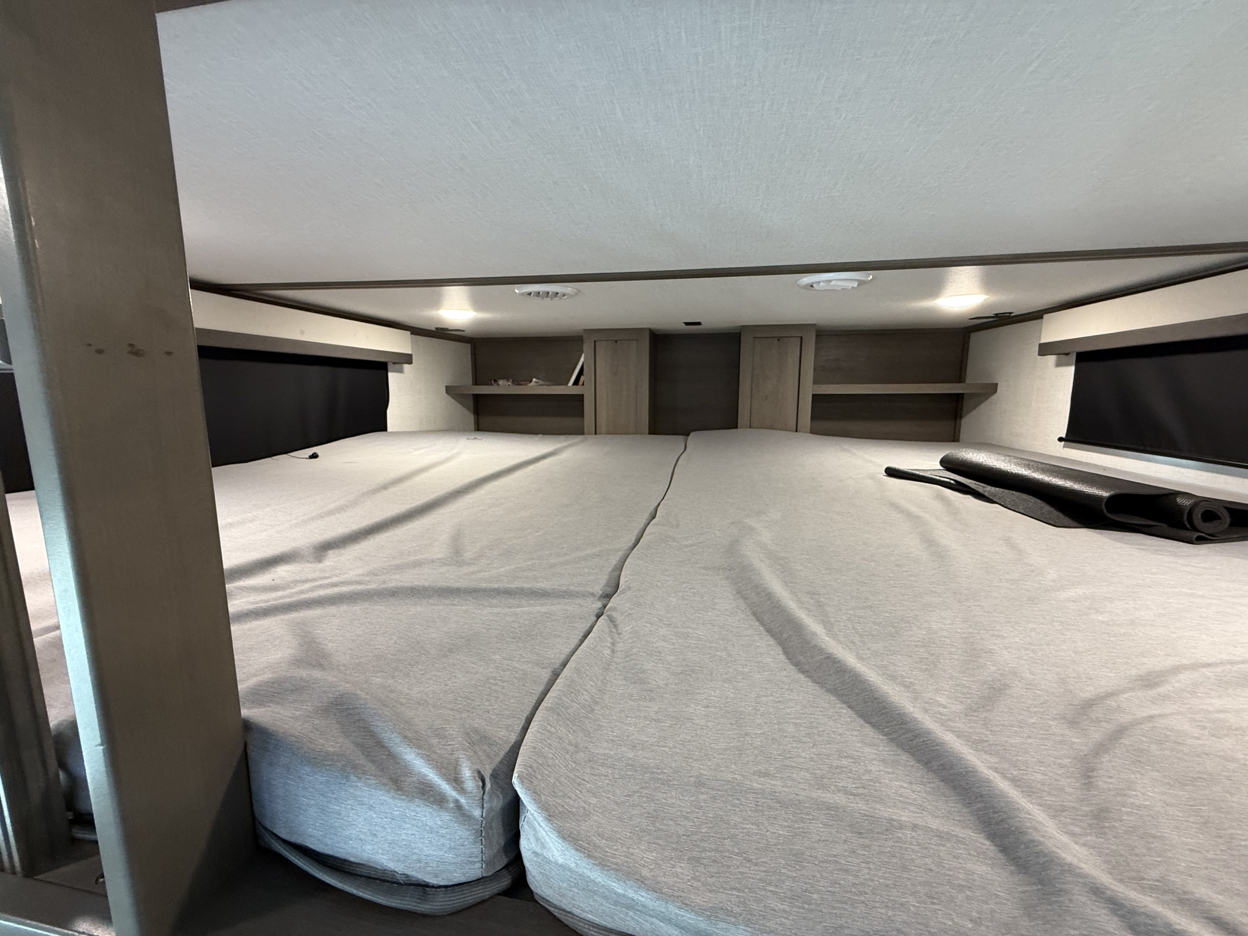 Inside an RV rental: a large, comfortable sleeping area with split mattresses, overhead storage, and ambient lighting.. Grand Design Solitude 2023