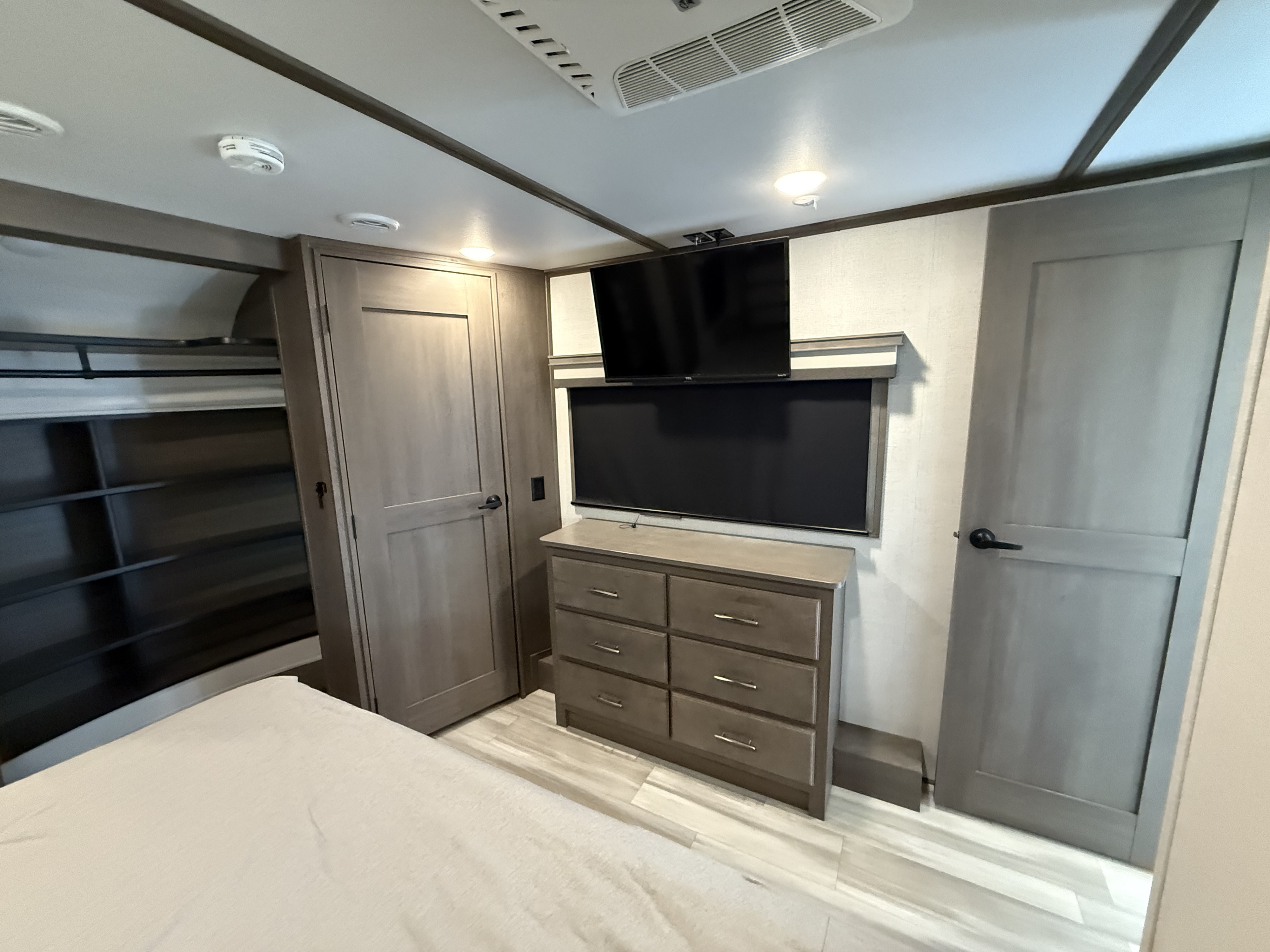 Modern RV rental bedroom with comfortable bed, mounted TV, retractable screen, dresser, and storage. Ready for your trip!. Grand Design Solitude 2023