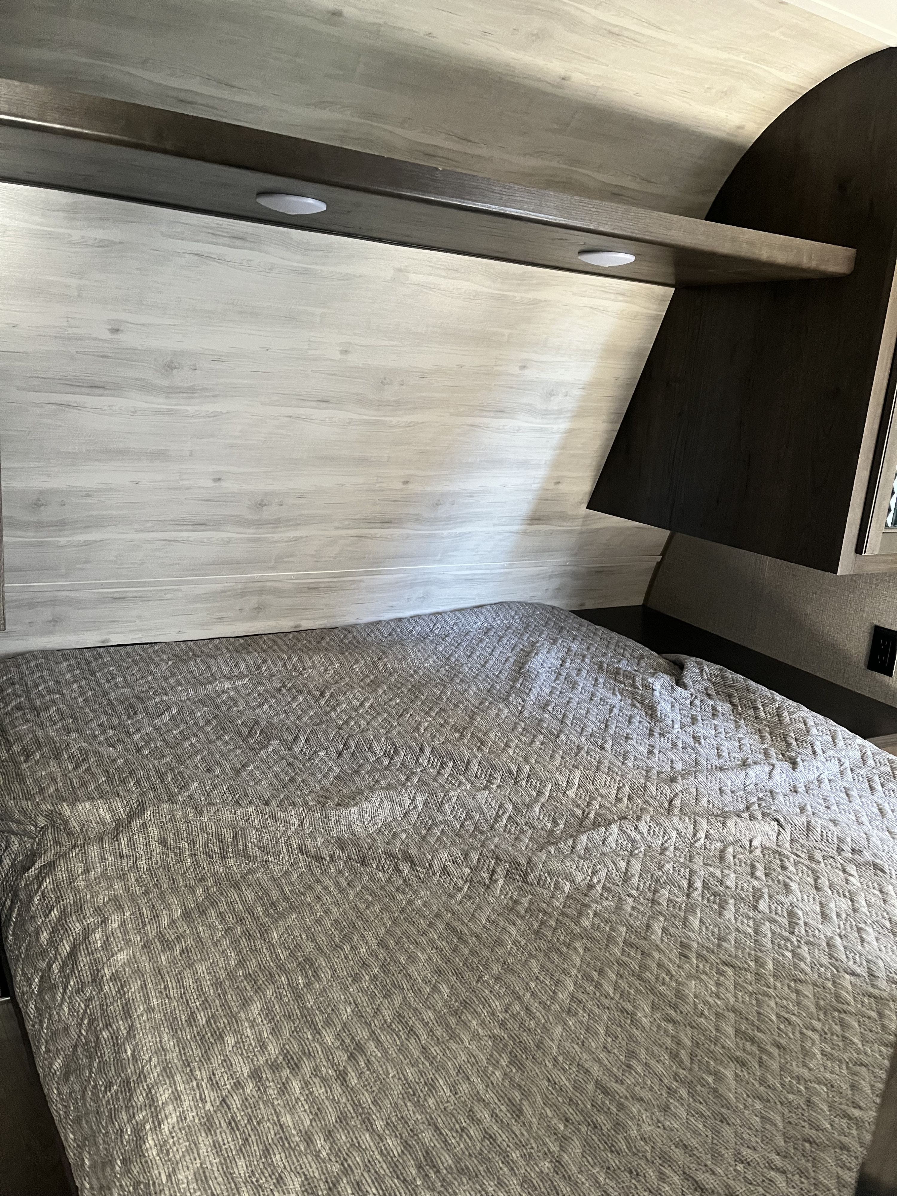 Cozy RV rental bedroom featuring a quilted bedspread, light wood headboard, and handy overhead shelf with lights.. Jayco Jay Flight SLX Rocky Mountain Edition 2021