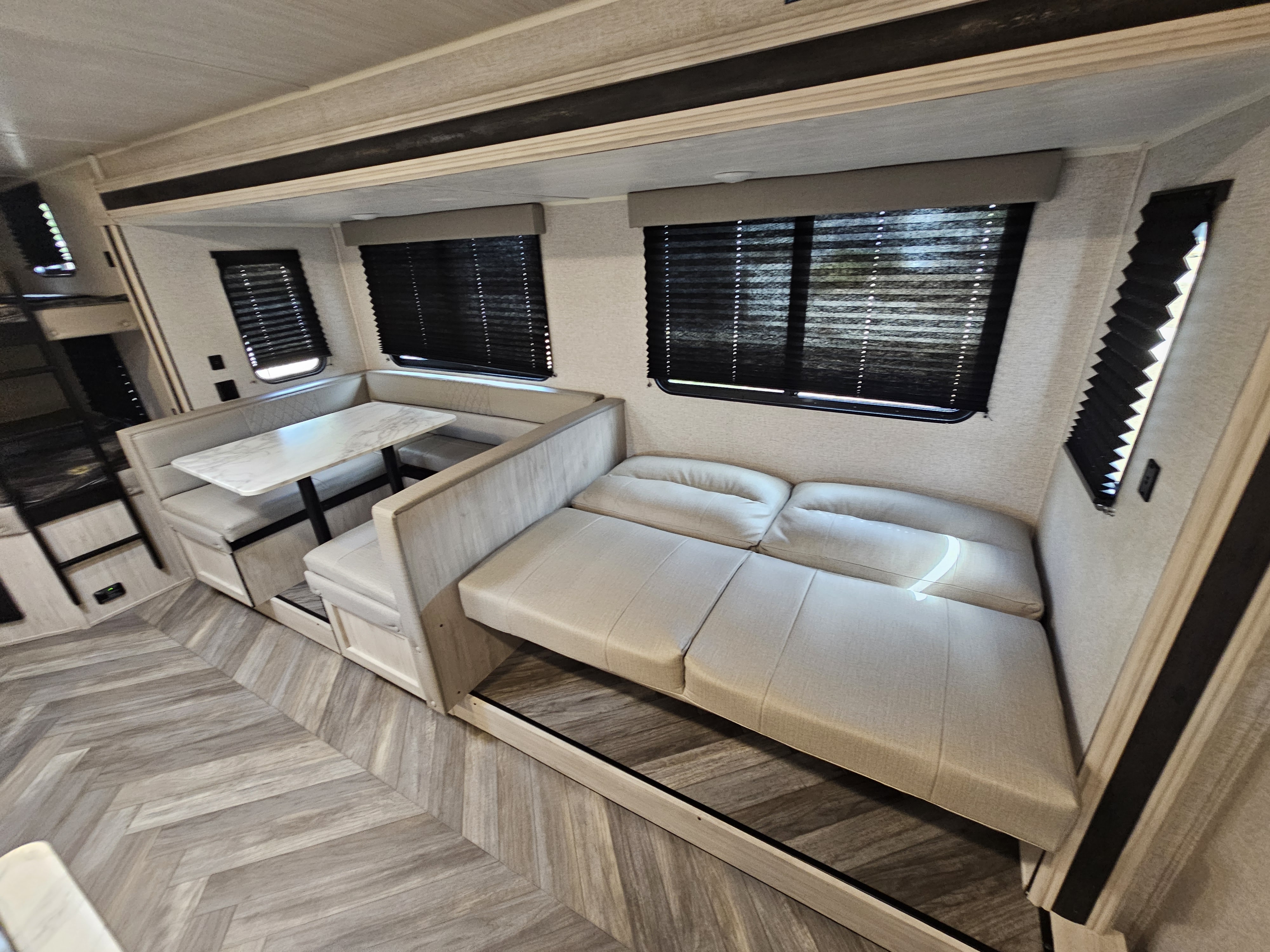 Inside a modern RV rental: dinette, sofa bed, and bunk beds. Light decor, herringbone flooring. Perfect for family trips.. East to West Della Terra LE 2023