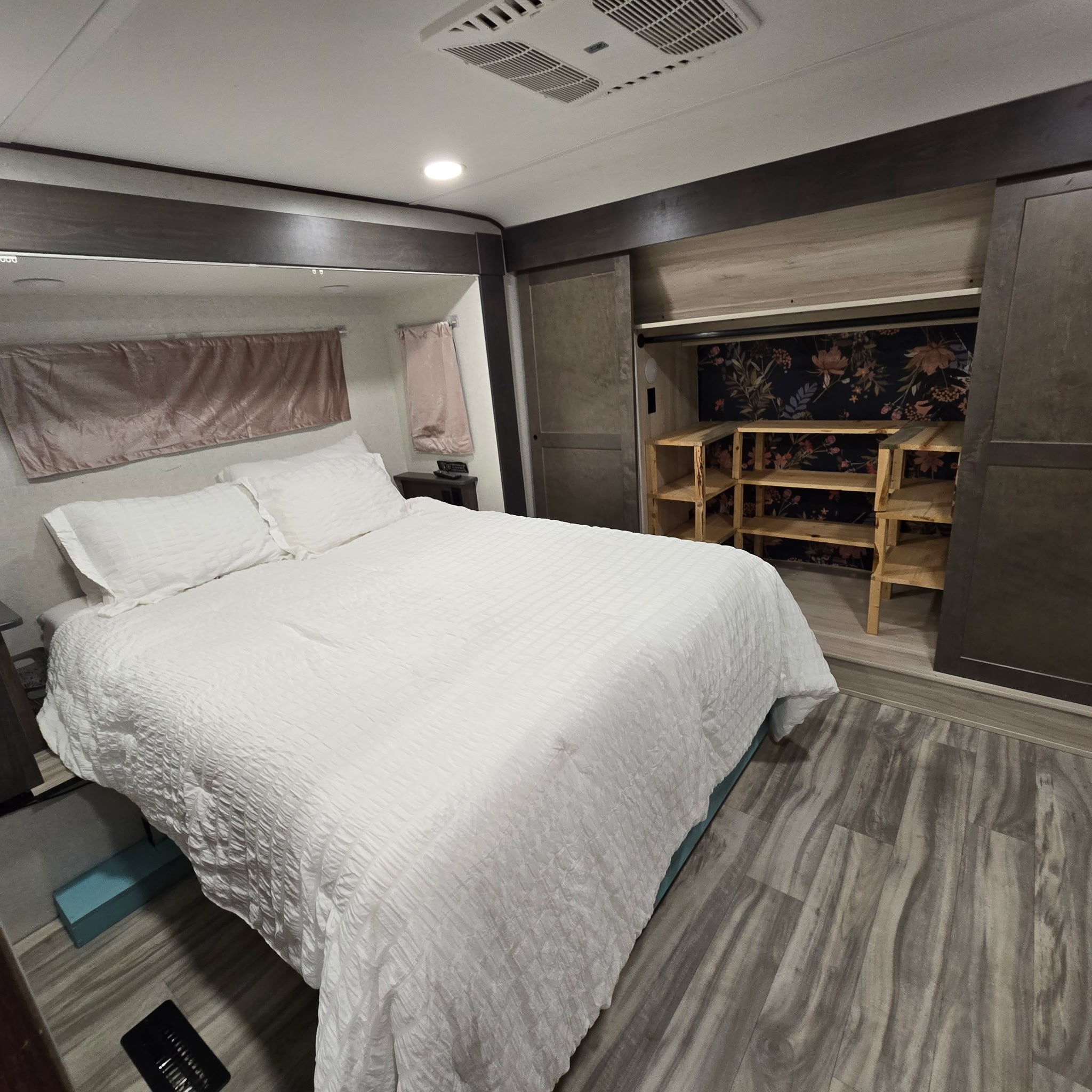 Interior of an RV rental bedroom with a white bed, floral accent closet, and grey wood floor. Ready for your trip.. Alliance RV Valor 2022