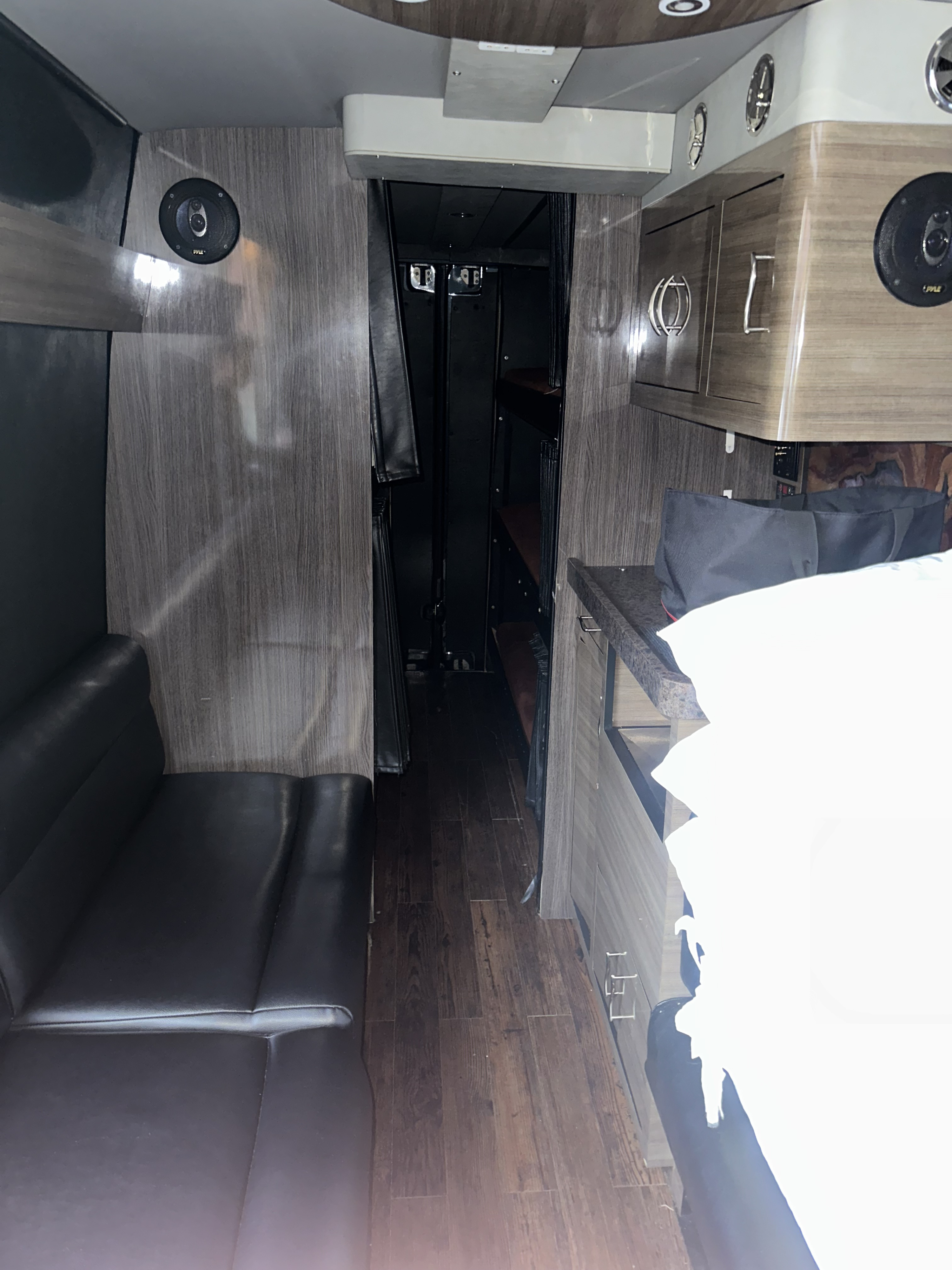 Spacious RV rental interior featuring a comfy black sofa, wood-grain cabinets, and a rear living/sleeping area. Modern camper van luxury.. Mercedes 3500 2013