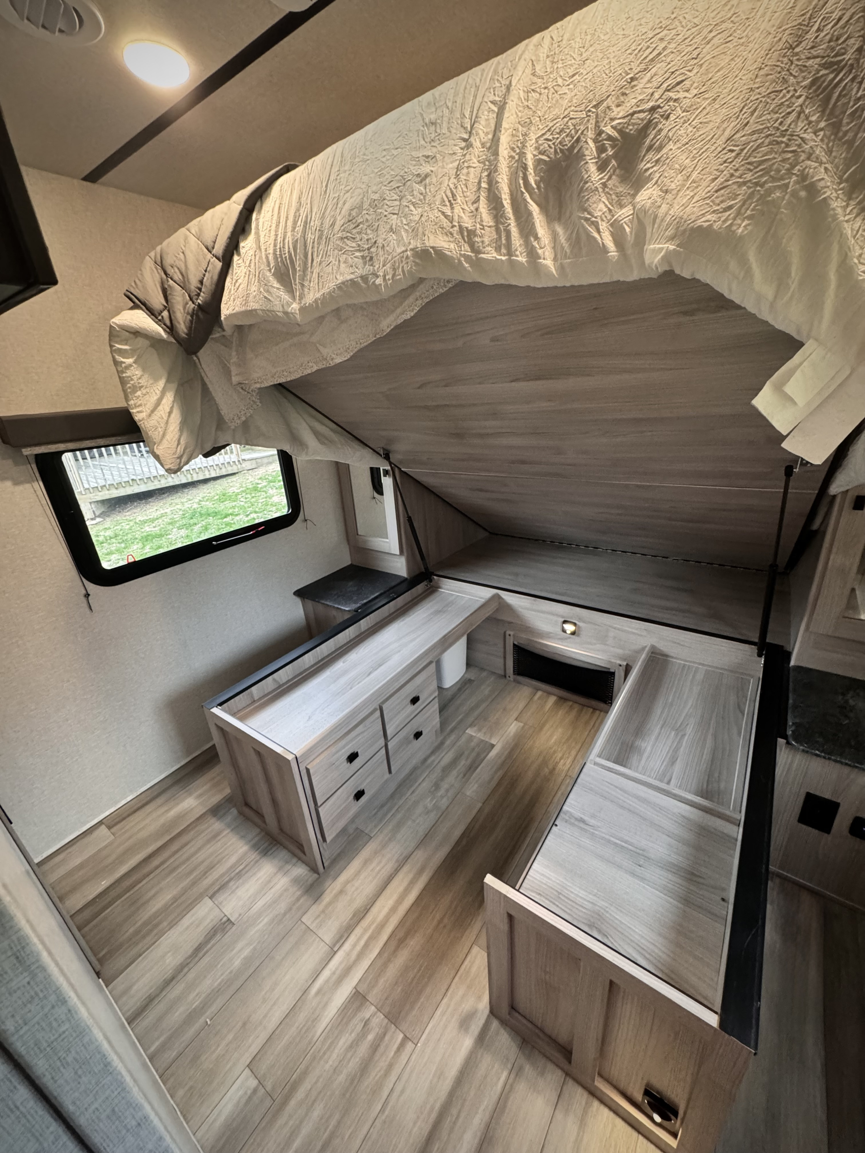 RV rental: Bed lifted to reveal under-bed storage, wooden cabinets, and light wood-look flooring in a compact interior.. Forest River Coachmen Northern Spirit Ultra Lite 2023