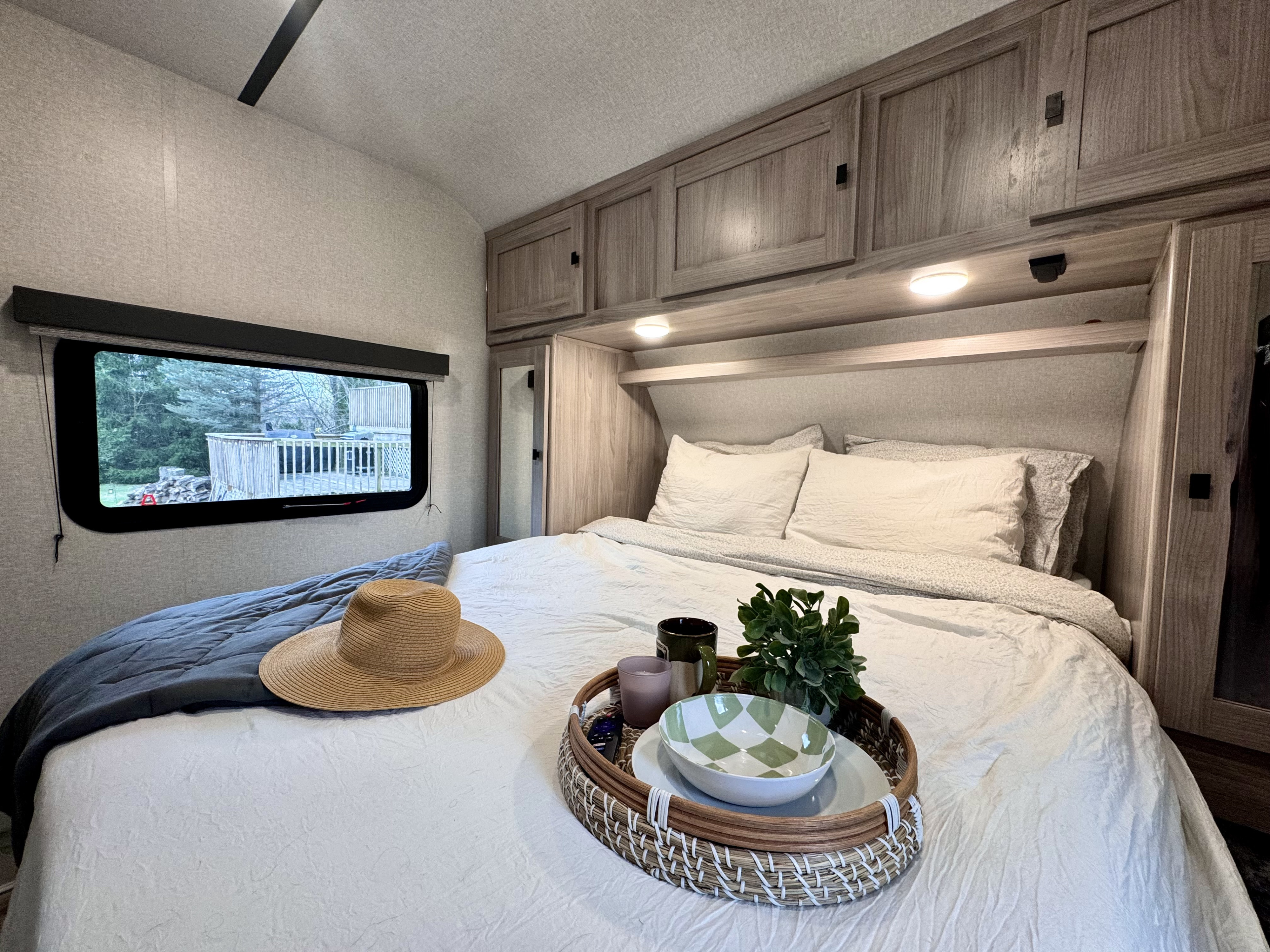 Inviting RV rental bedroom with a neatly made bed, decorative tray, overhead storage, and window showcasing the outdoors.. Forest River Coachmen Northern Spirit Ultra Lite 2023