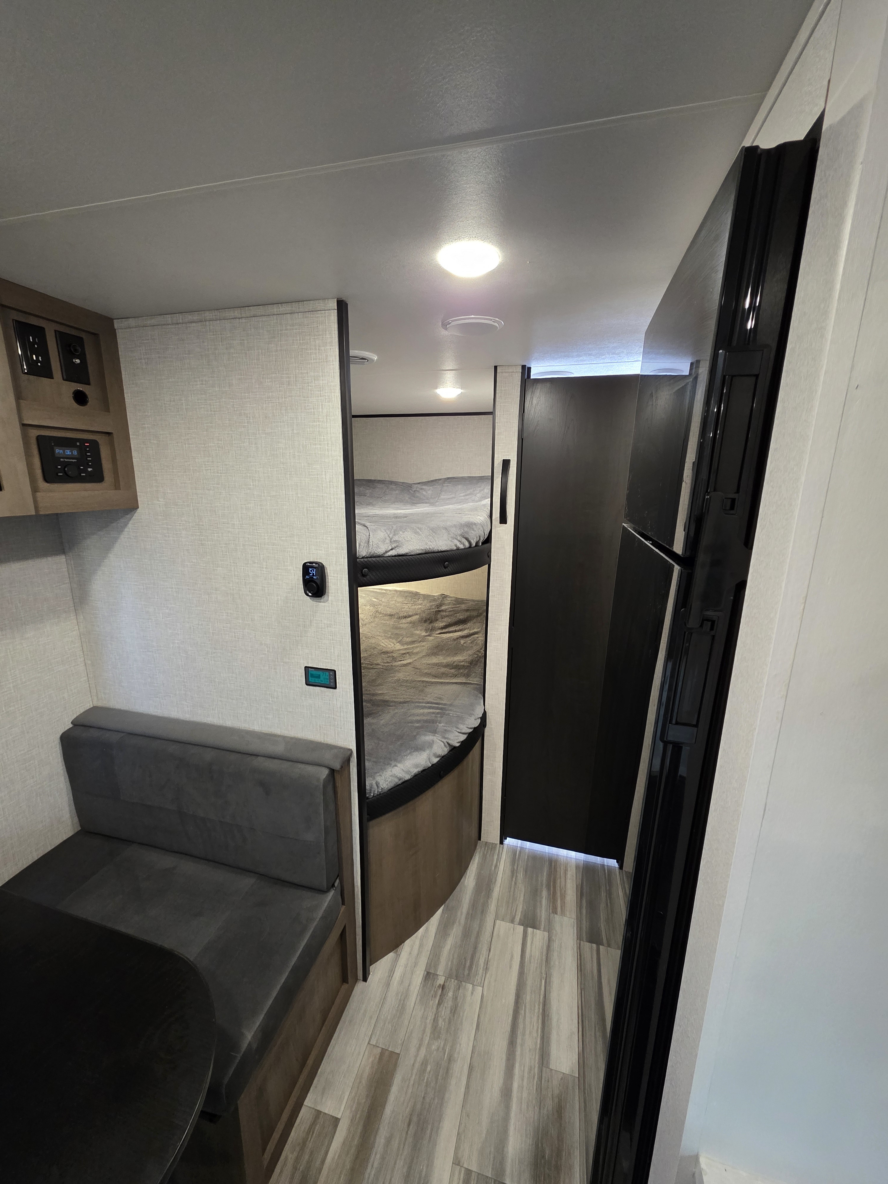 Interior view of an RV rental showing a dining booth, control panel, bunk beds, and refrigerator, with wood-look flooring.. Jayco Jay Flight 2025
