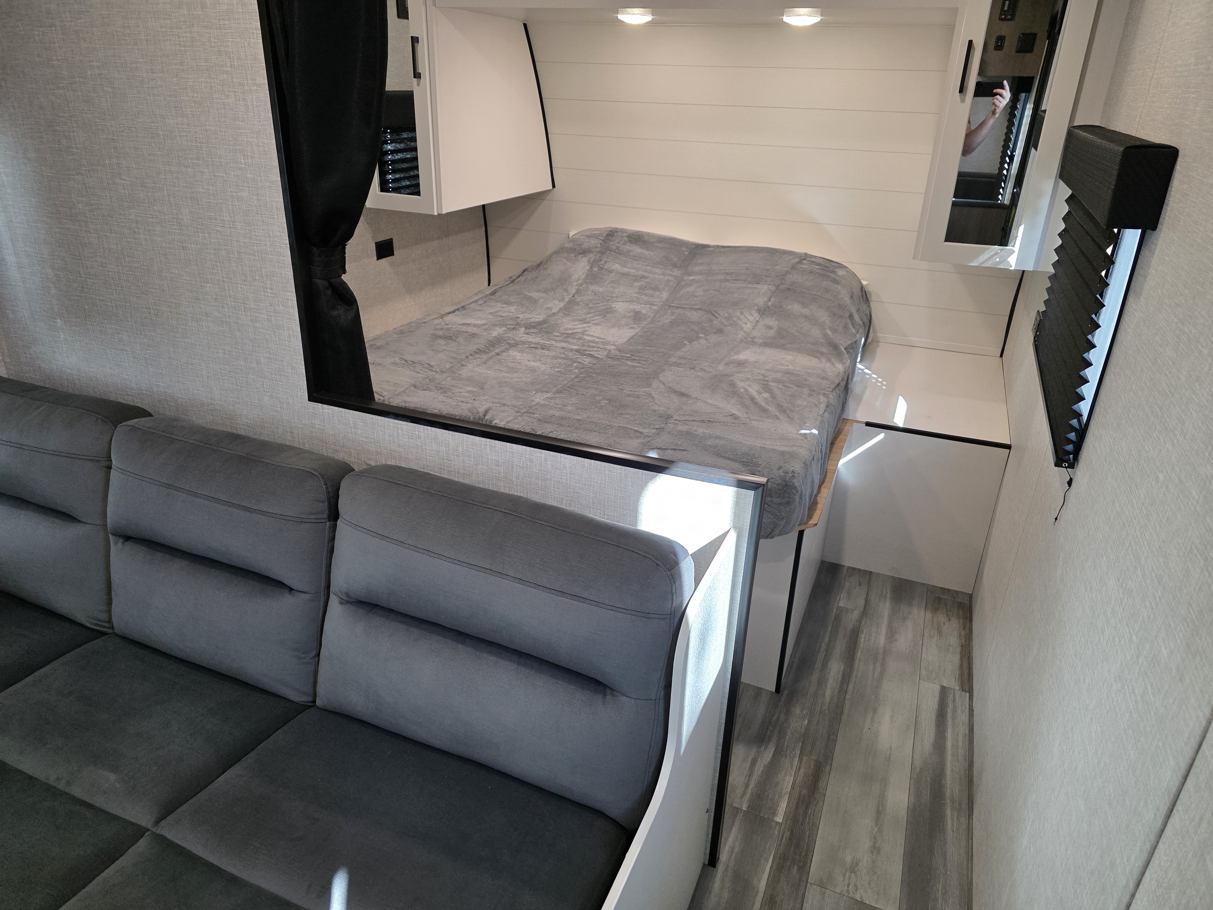 RV rental interior: A gray sofa on the left, an elevated bed with a gray blanket, and overhead storage in a compact space.. Jayco Jay Flight 2025
