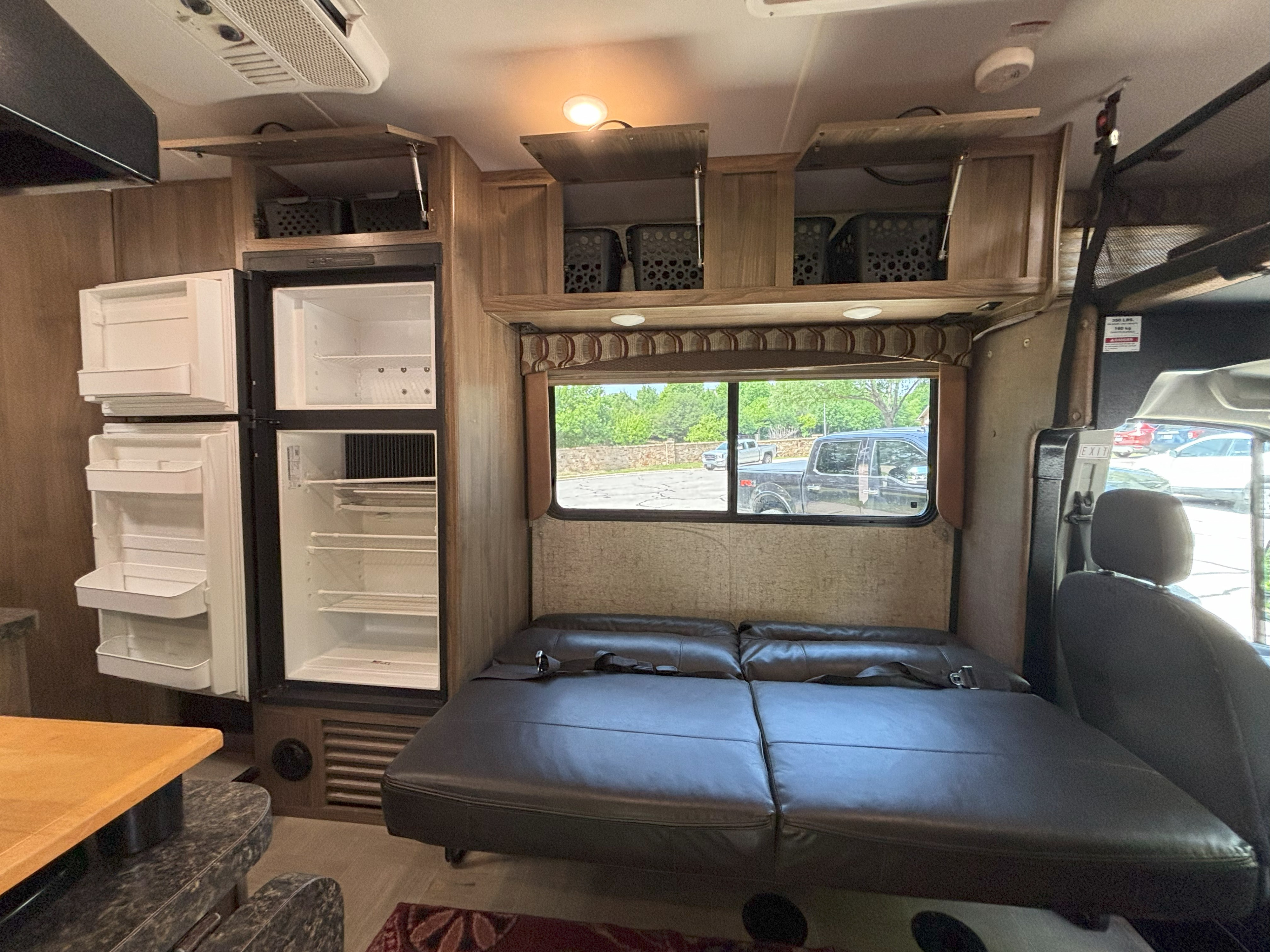 Clean RV rental interior: large empty fridge, modular sofa/bed with seatbelts, open overhead cabinets with storage.. Forest River Coachmen Freelander Micro 2018
