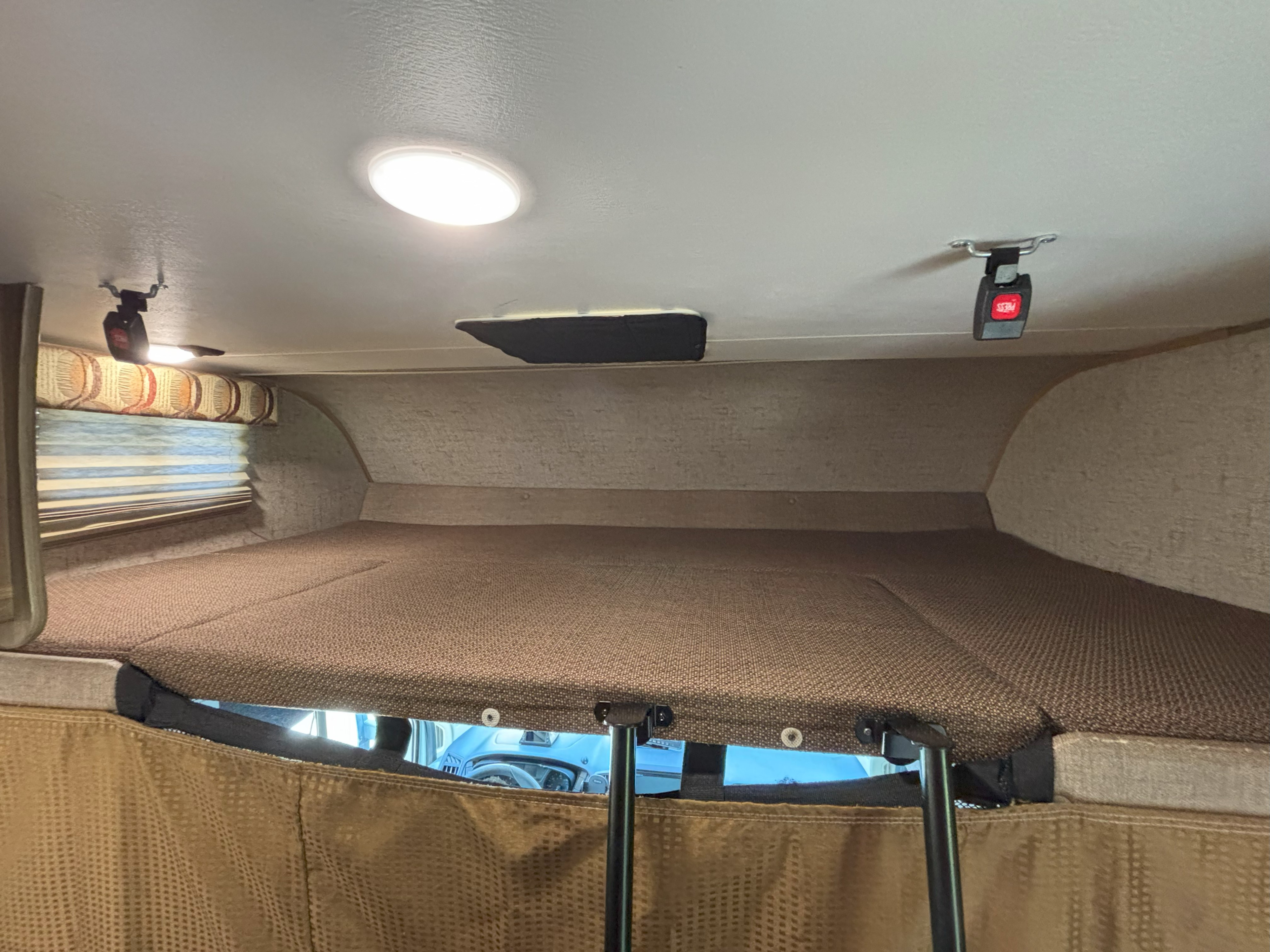 Cozy overhead bunk bed in an RV rental. Features include brown cushions, ceiling lights, safety buckles, and a ladder.. Forest River Coachmen Freelander Micro 2018