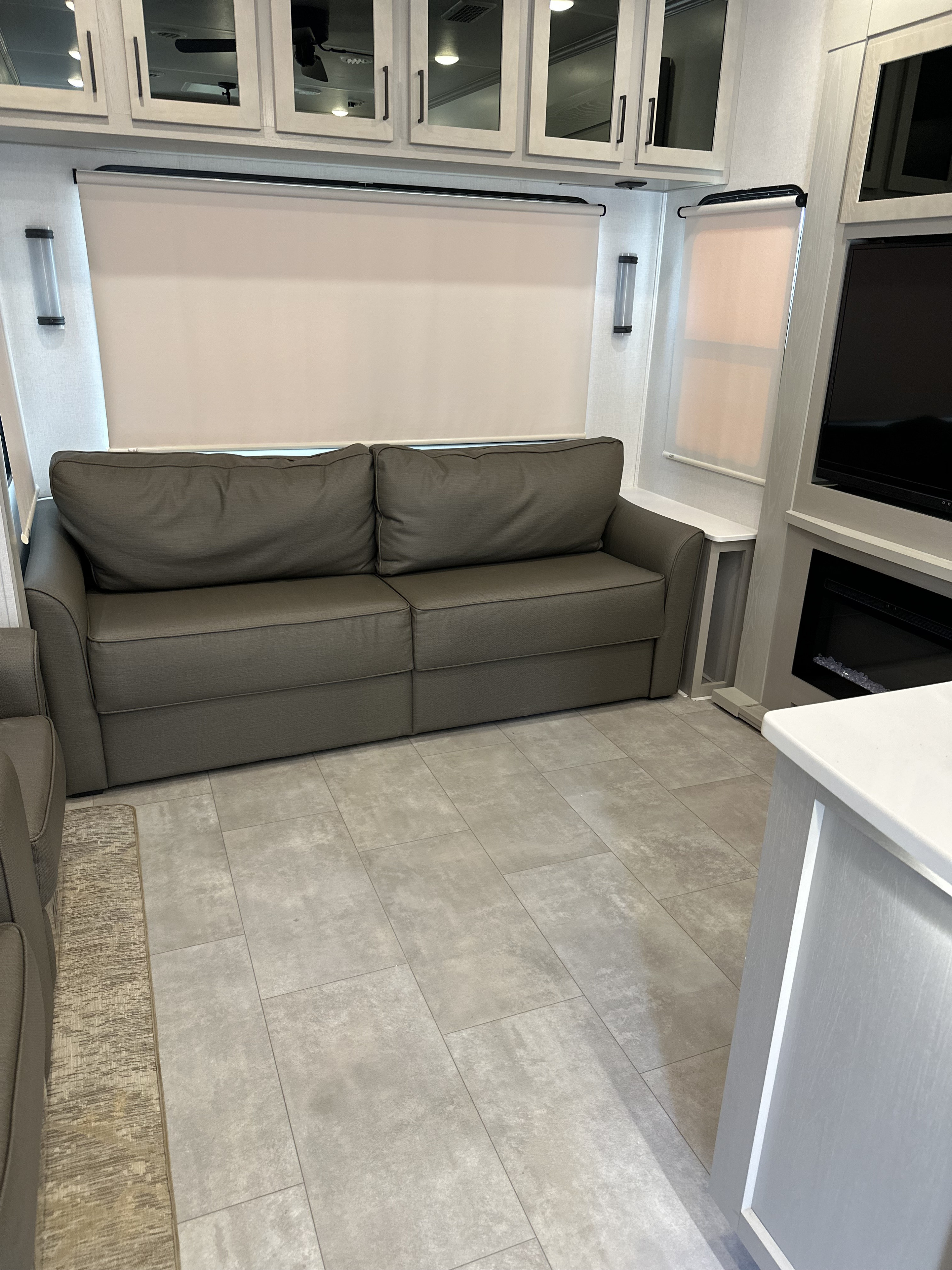 Modern RV rental interior featuring a gray sofa, light cabinets, tile flooring, roller shades, and a media console with fireplace.. Forest River Palomino Columbus C 2022
